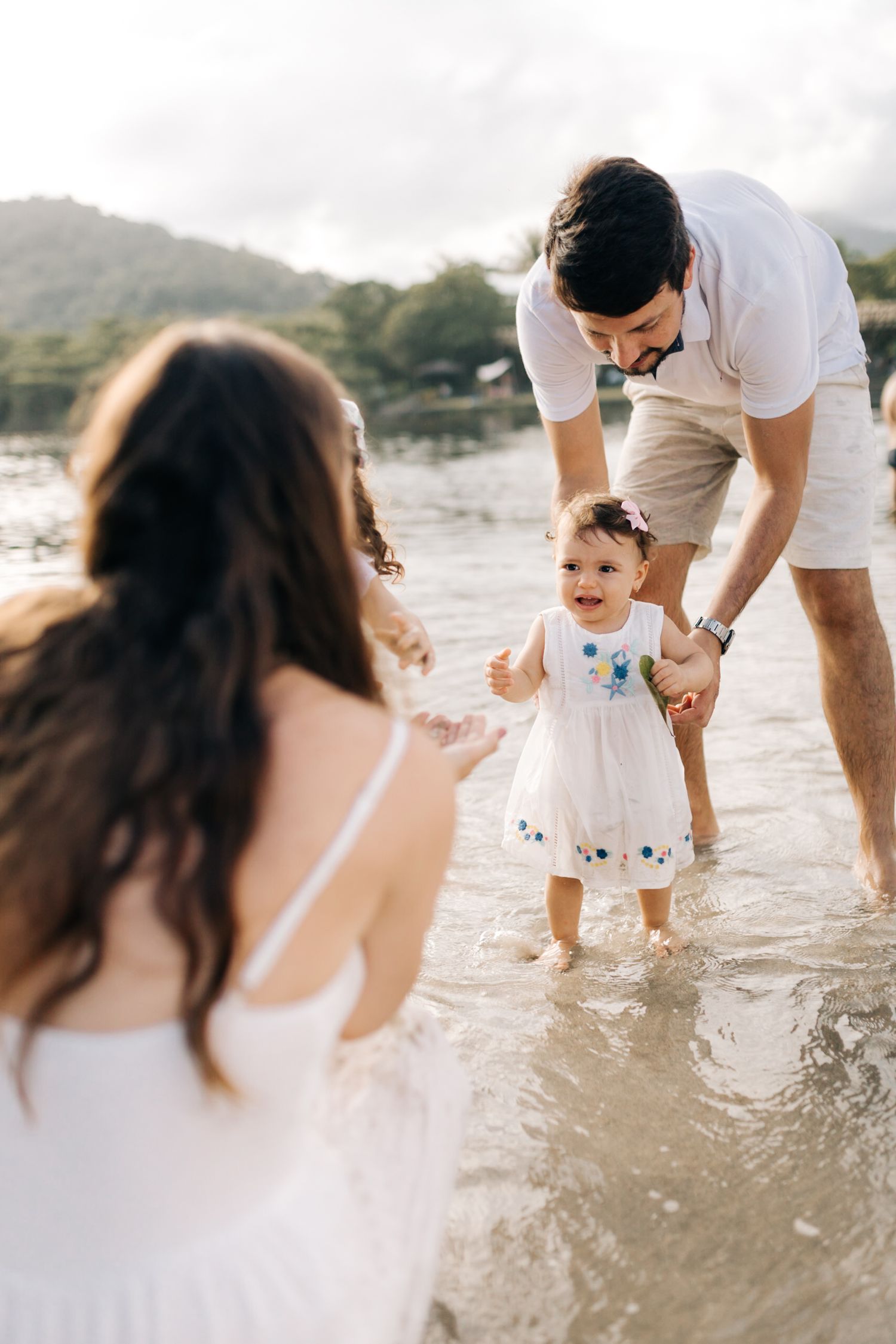 Family playing together in gentle ocean waves at a scenic beach during golden hour.