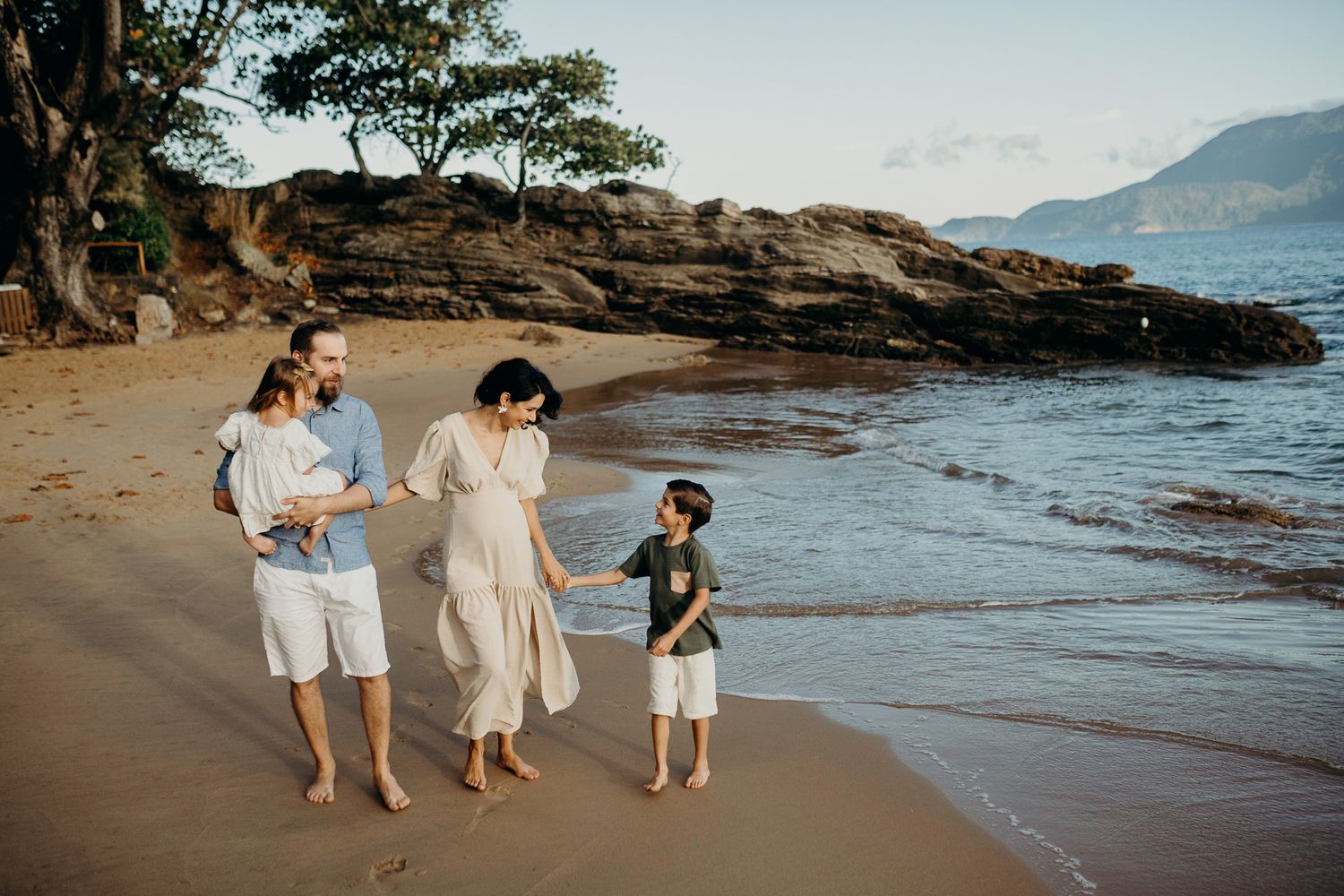 Family of three walking together on a scenic rocky beach during golden hour.