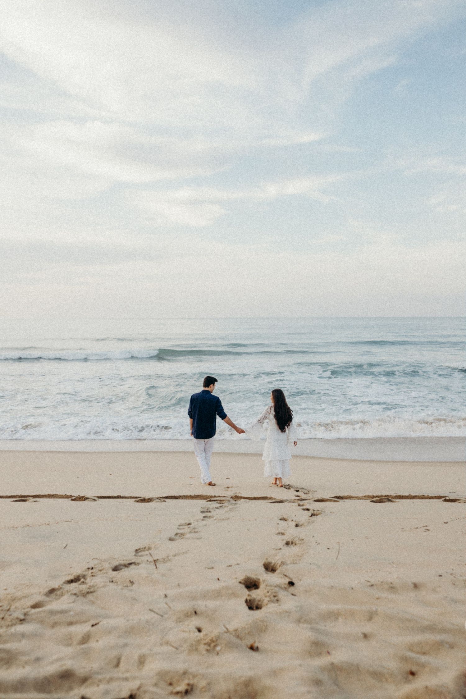 Couple holding hands while running together on a scenic beach with gentle waves rolling in.