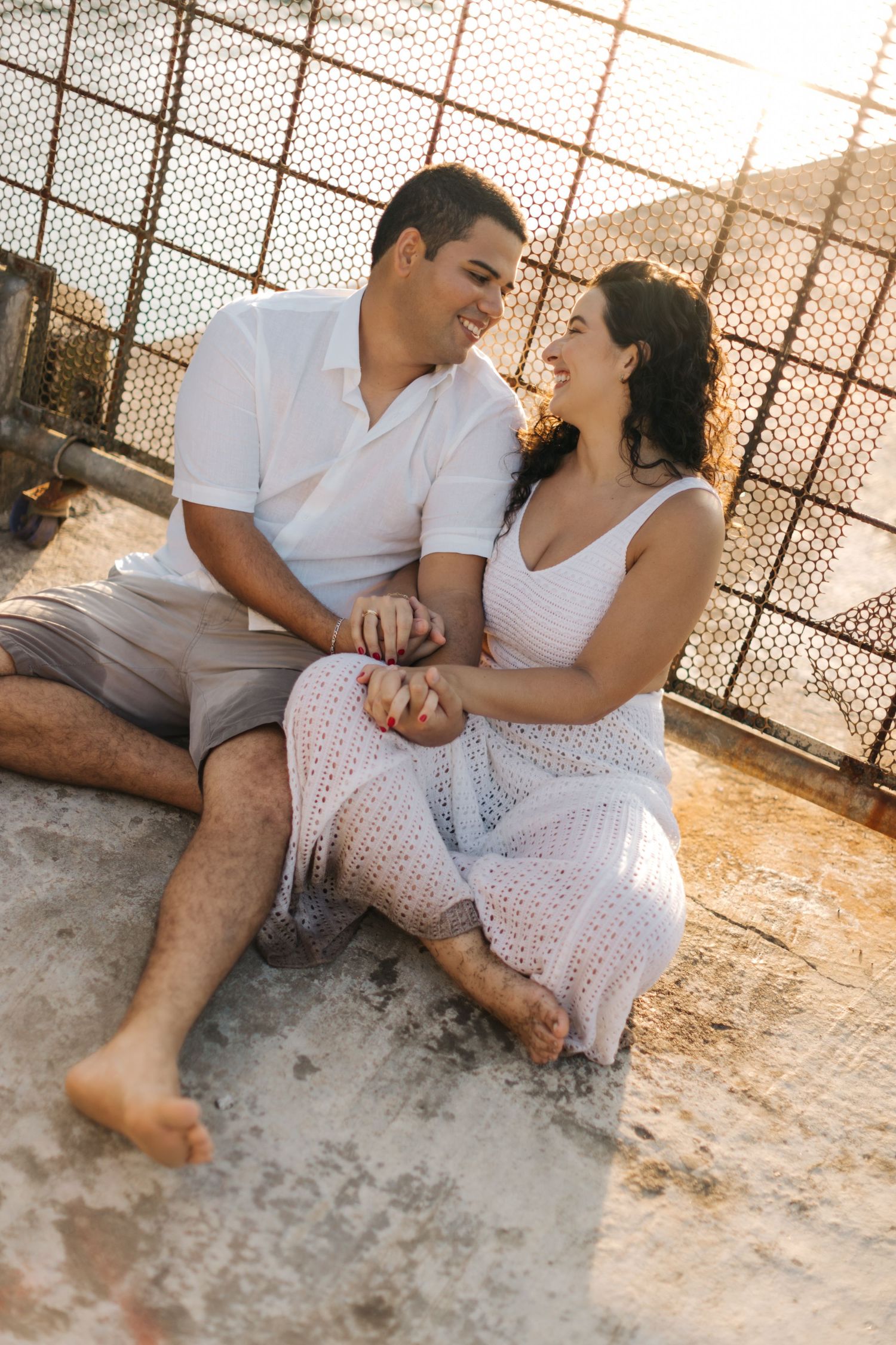 Couple sitting together on ground sharing intimate moment against industrial backdrop.