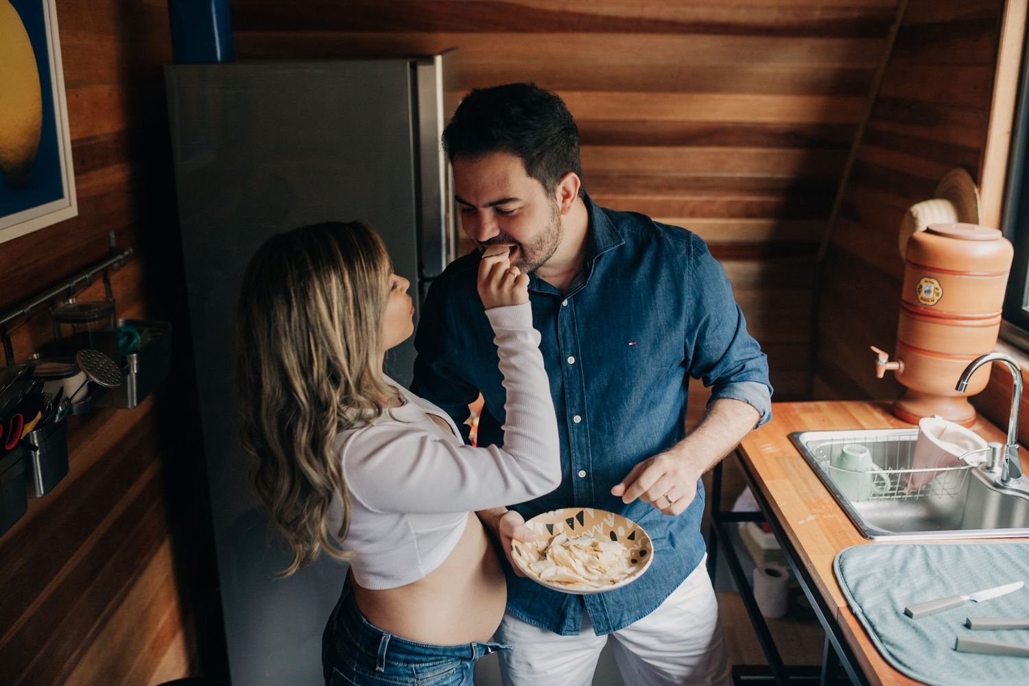 Couple laughing together while sharing snacks in a cabin with warm wooden walls.