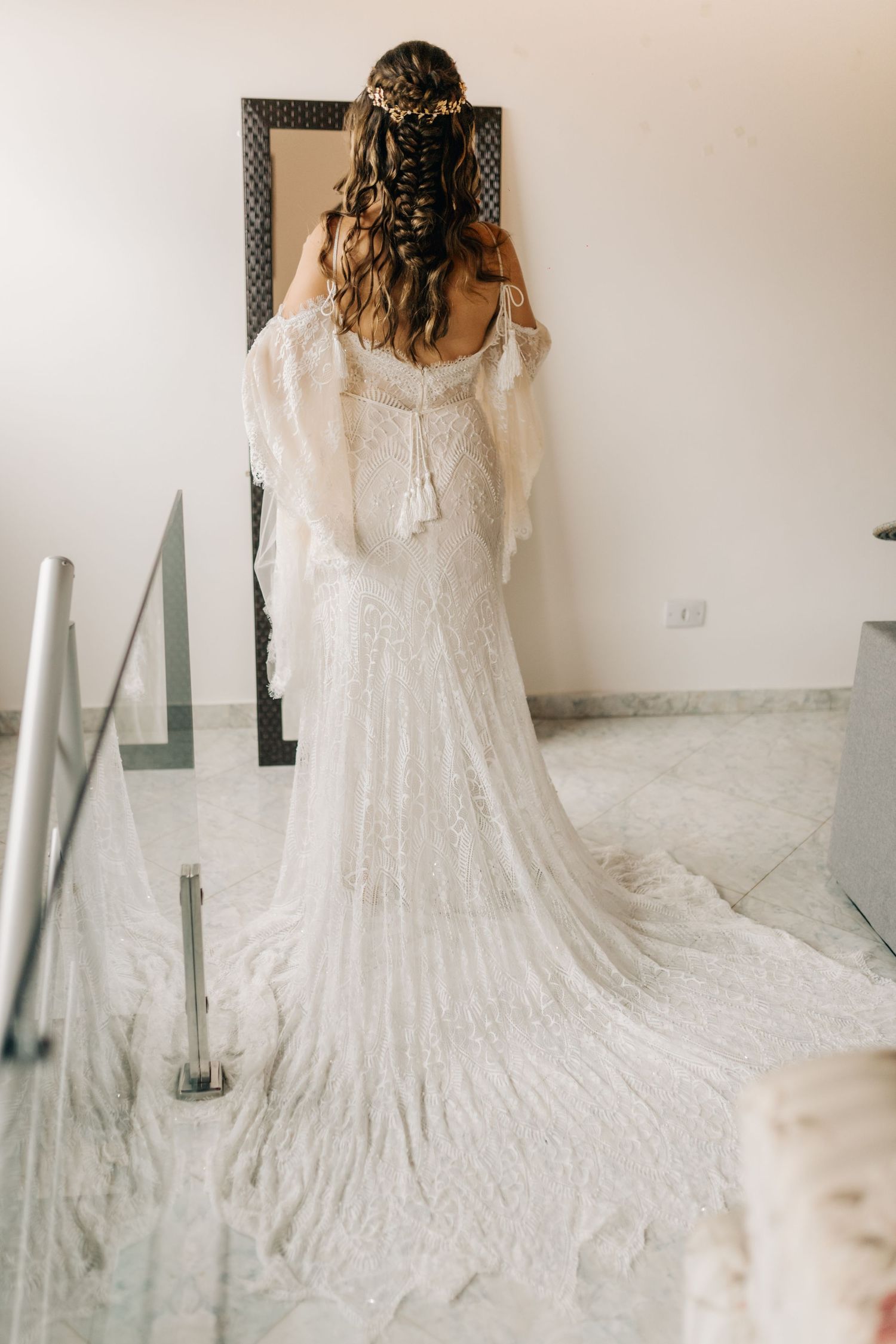 Full length back view of bridal gown with delicate lace train on marble floor.