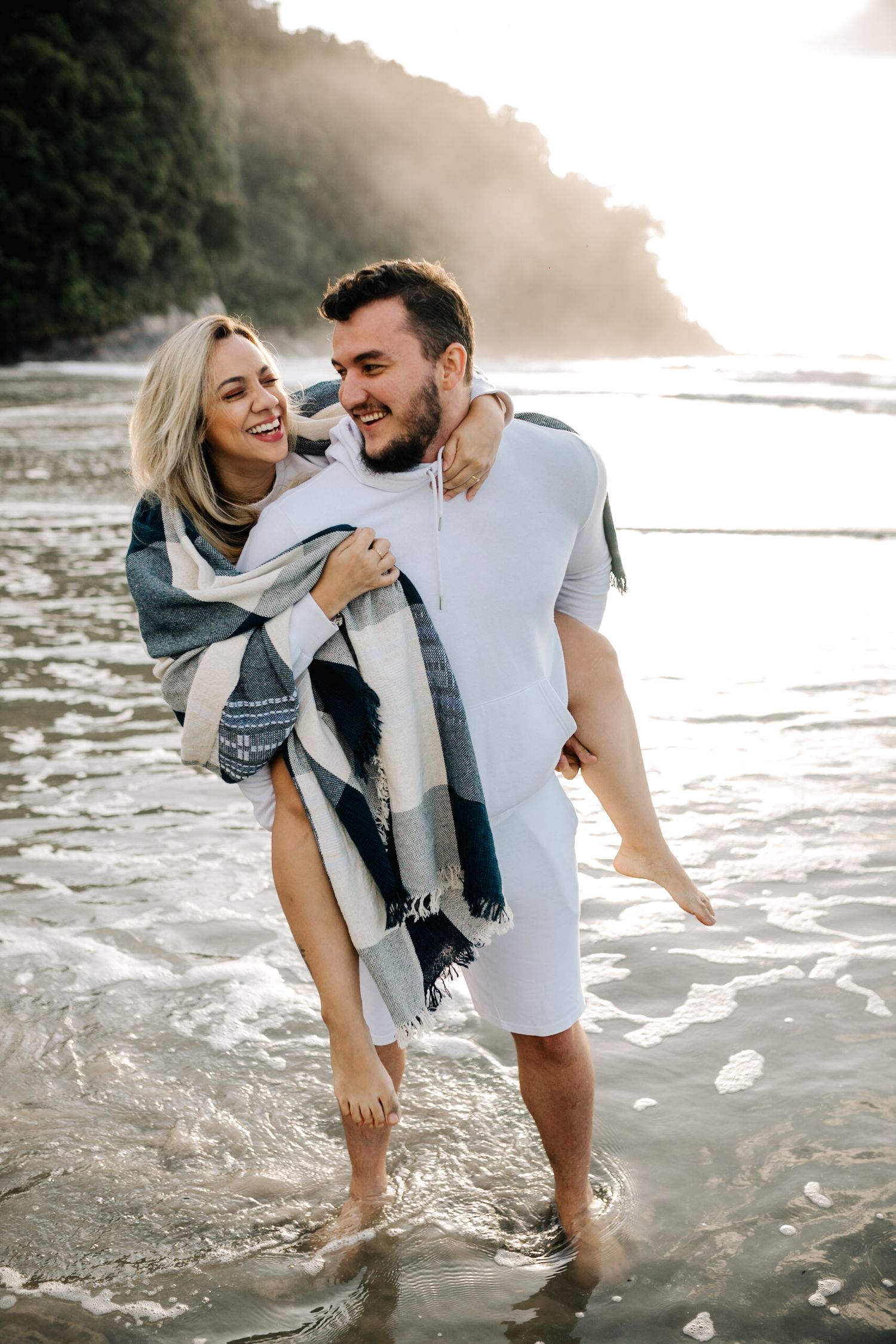 Happy couple embracing in shallow ocean waters during sunset beach photoshoot.