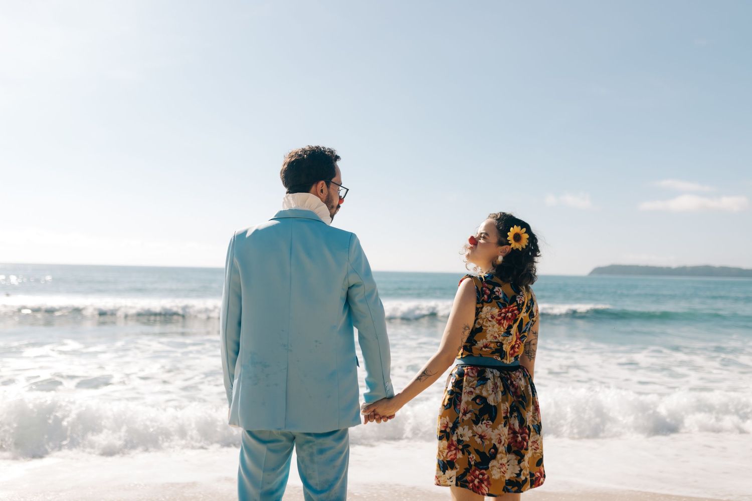 A couple in coordinated outfits gazes at the ocean waves on a bright beach day.