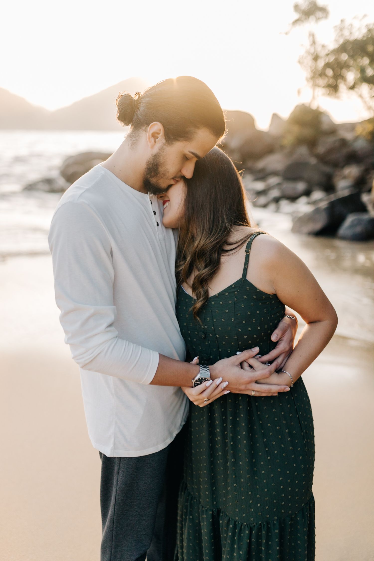 Tender moment captured between couple in coordinated outfits during sunset beach photoshoot.