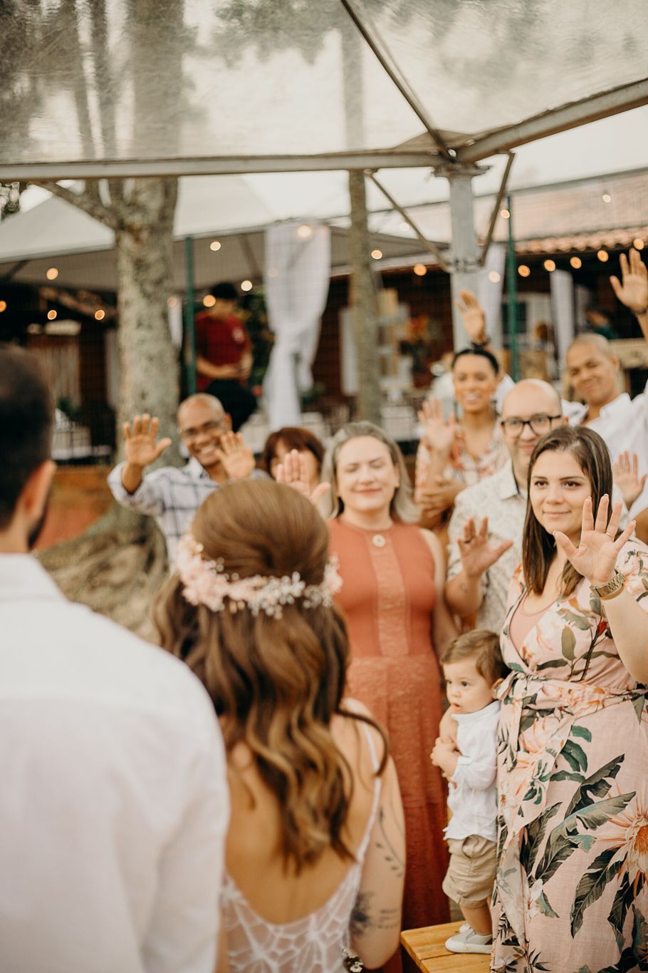 Wedding guests gather under a tent with string lights during an outdoor celebration.