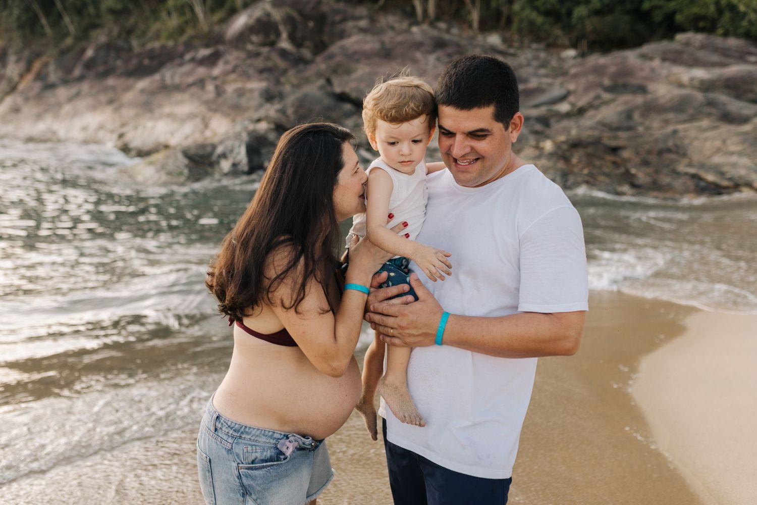 Family enjoying a playful moment together on a scenic beach with rocky cliffs in the background.