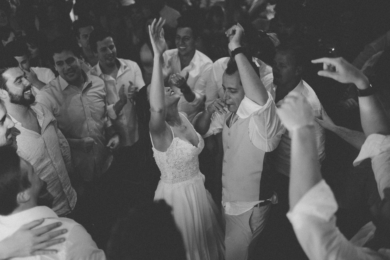 Black and white photo of wedding guests dancing with arms raised during a lively reception.