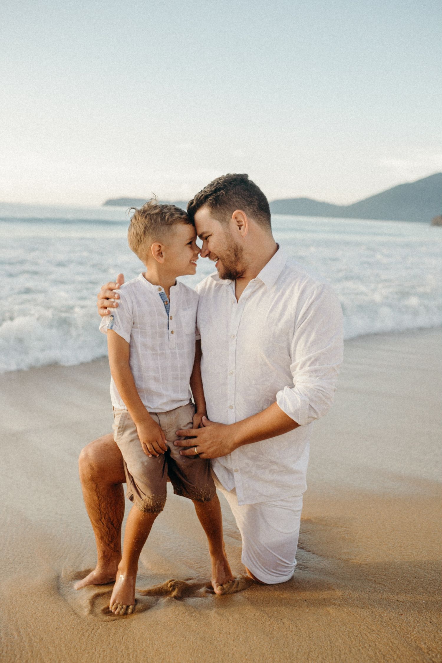 Parent and child share a tender moment while sitting on a sunny beach.