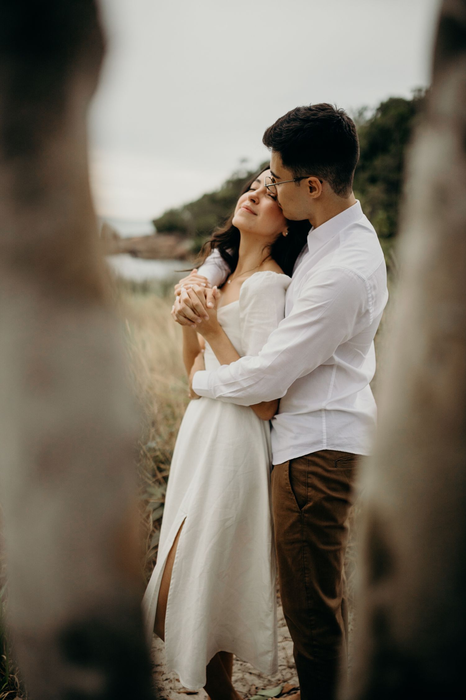 A couple embracing on a coastal hillside with soft lighting and natural scenery.