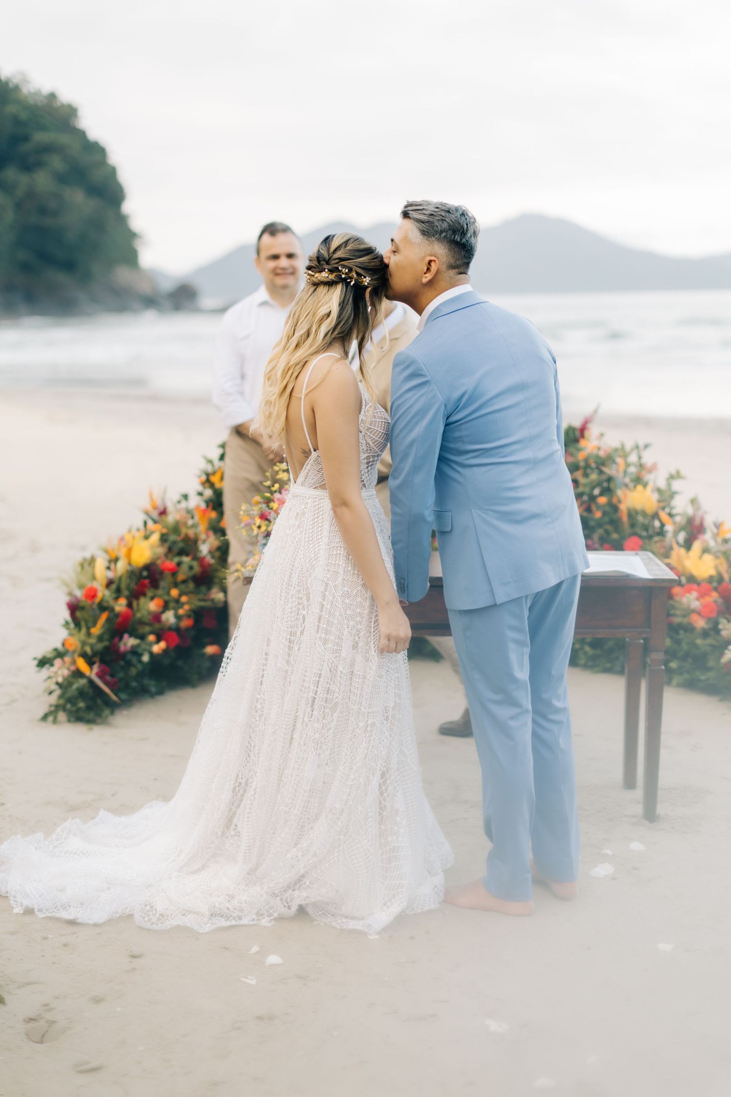 Intimate beachside wedding moment with coastal mountains and colorful florals.