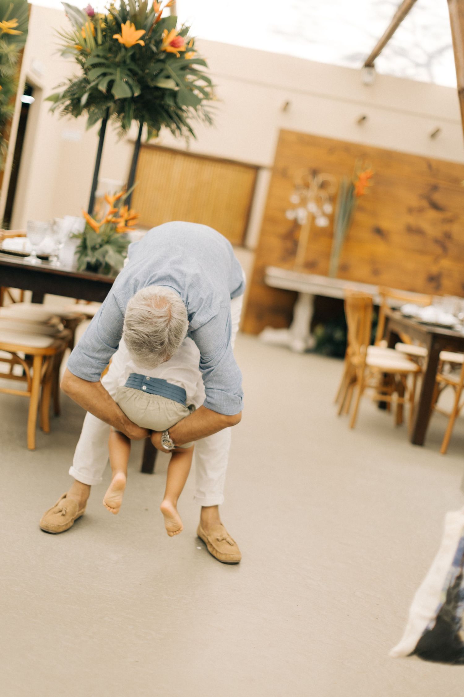 Someone in casual attire bends down in an indoor space with wooden furniture.