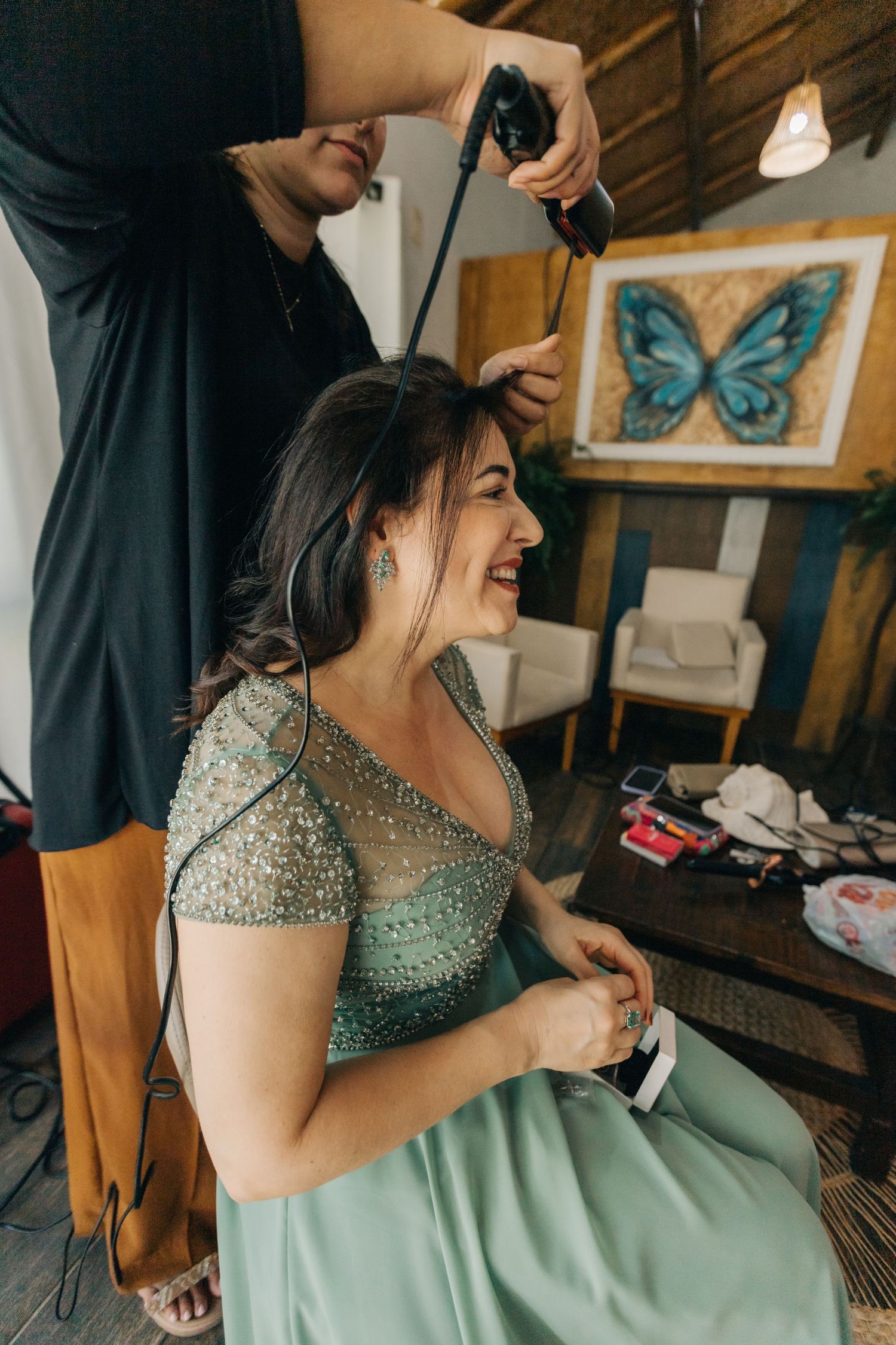A person in a mint green sparkly dress getting their hair styled in a rustic room with butterfly decor.