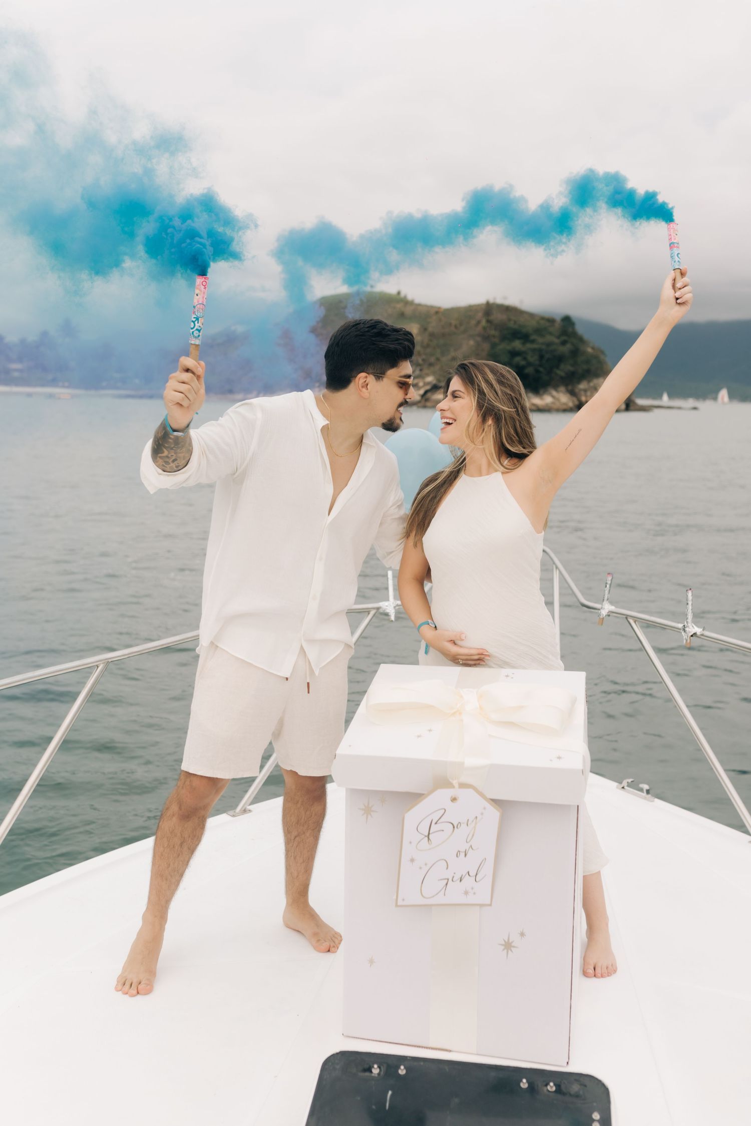 Couple holding blue smoke flares while celebrating on yacht with mountains in background.