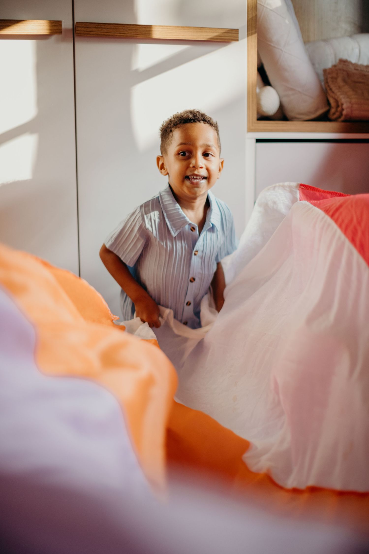 Young child in striped shirt smiling while playing among colorful fabrics.