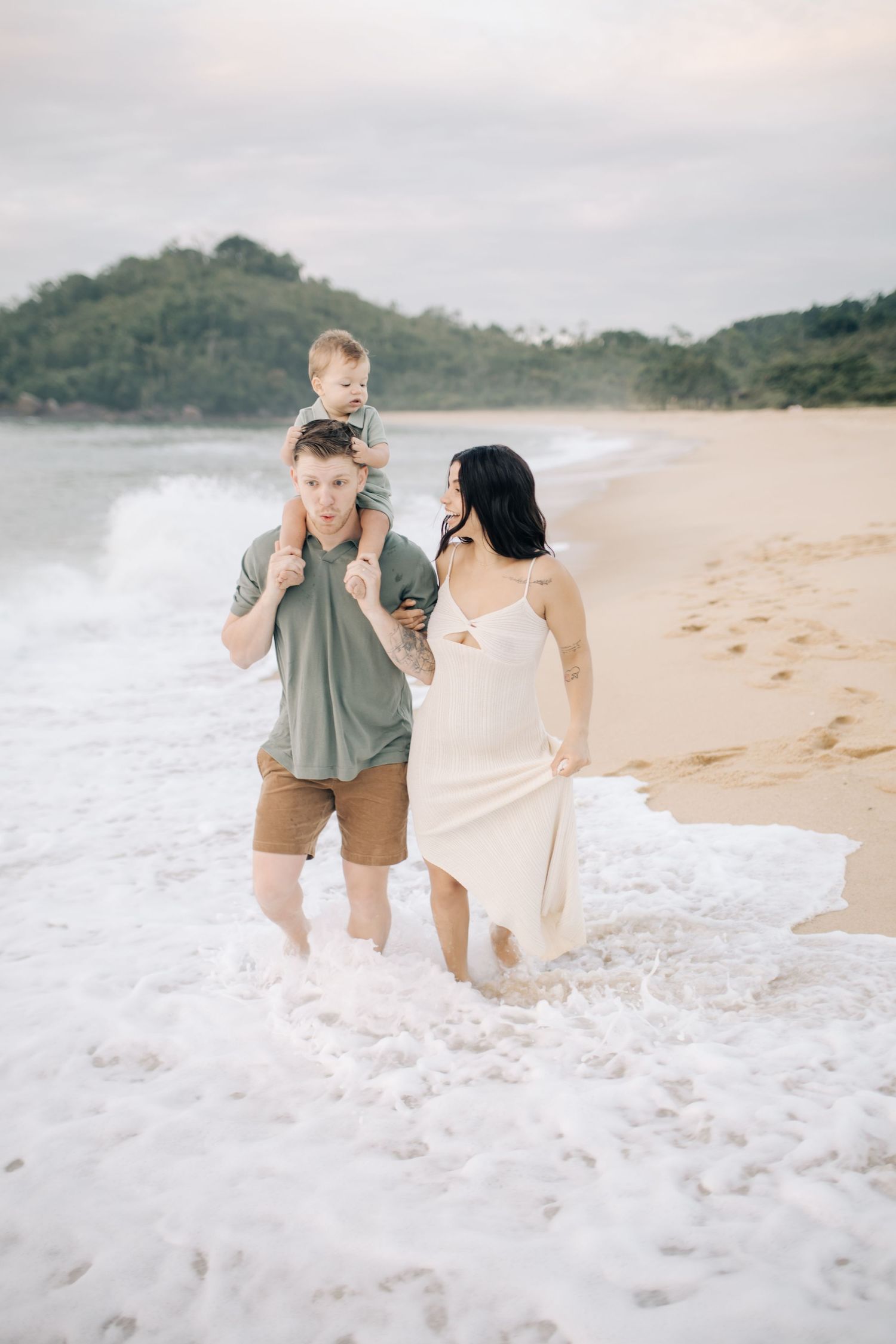 A family enjoys the waves together on a scenic beach with mountains in the distance.