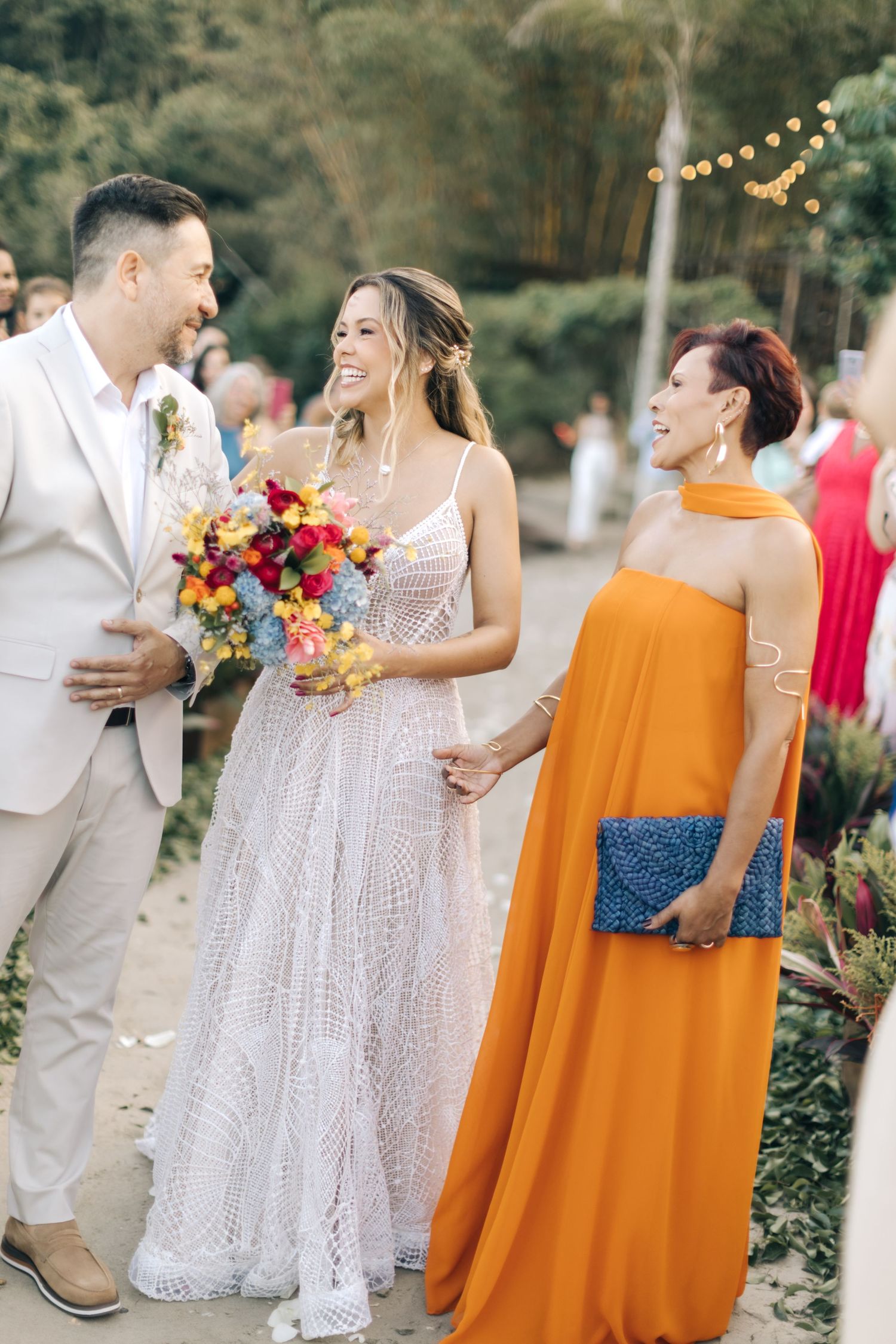 Happy wedding celebration on outdoor path with elegant white dress and vivid orange gown.