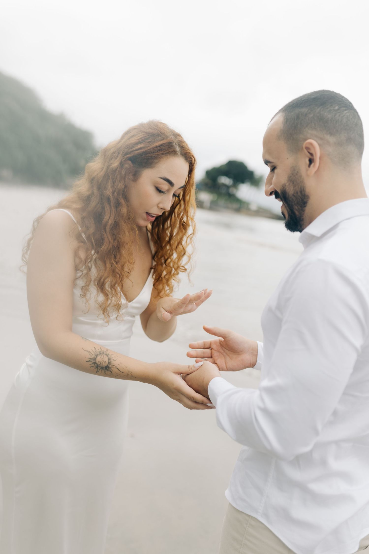 Tender exchange between two people in white attire on misty beach.