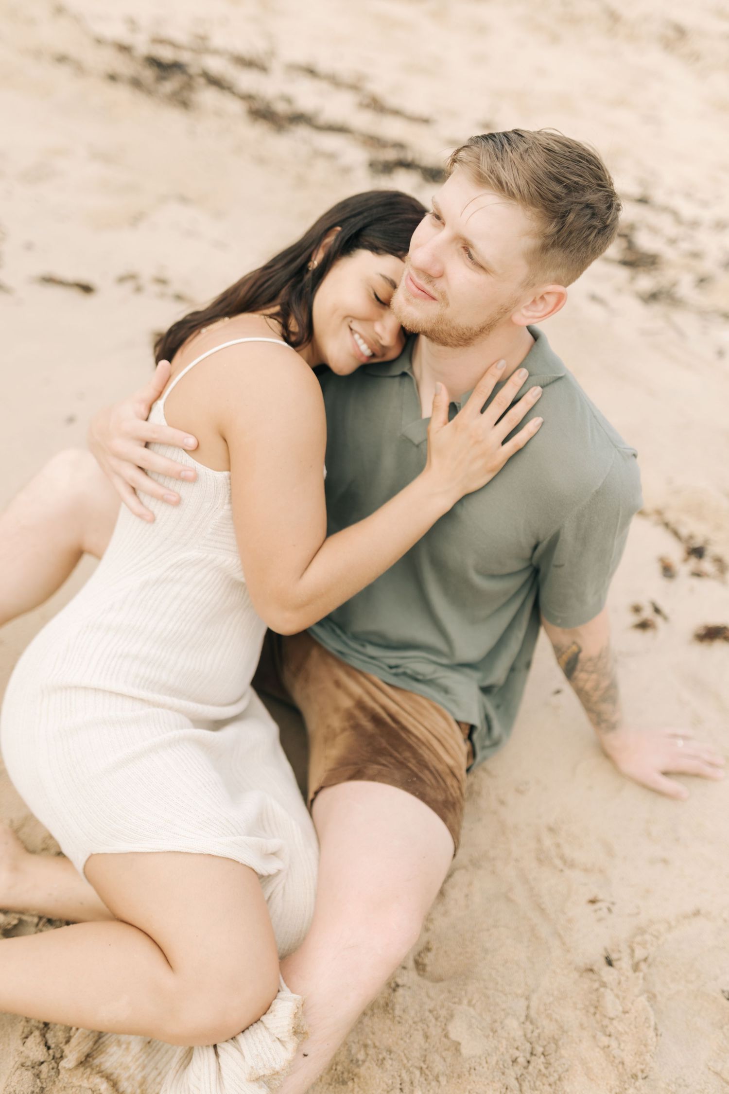 Intimate couple embracing on beach sand during golden hour photography session.