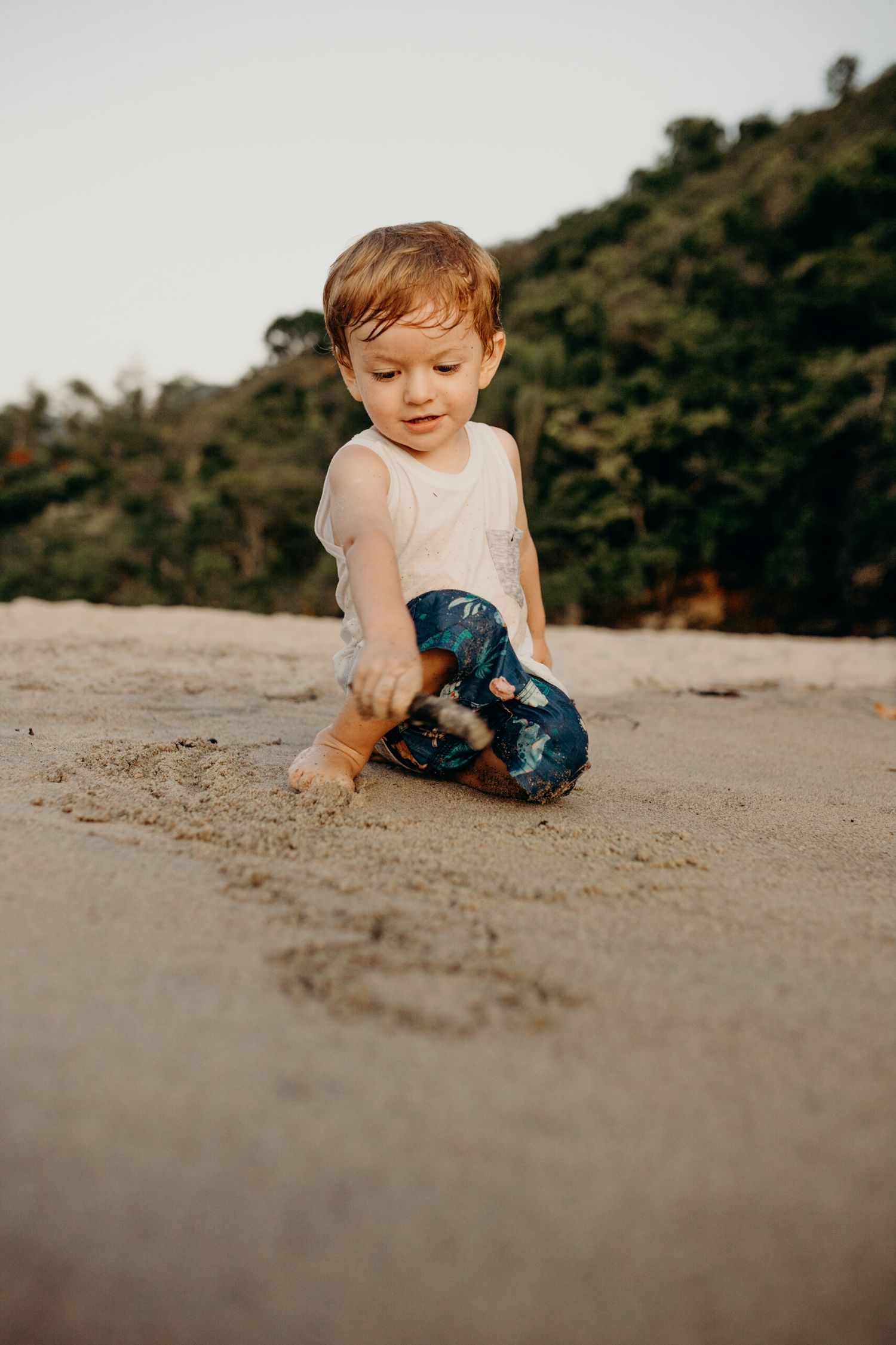 Child playing in the sand at a beach with mountains visible in the background.