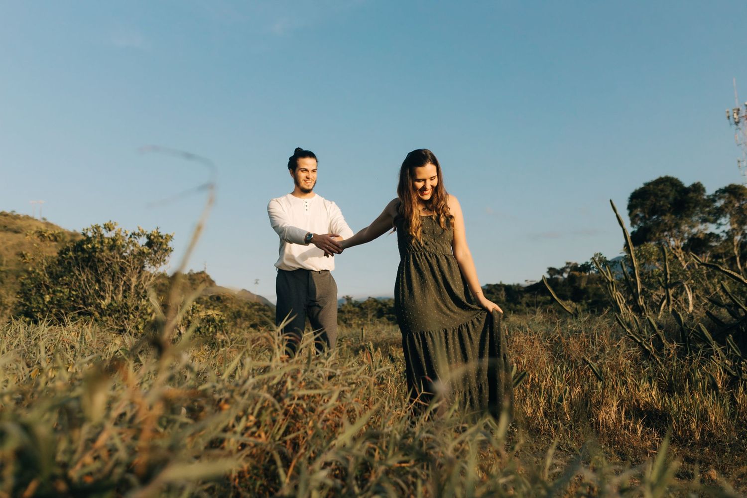 A couple stands together in a golden grass field during sunset.