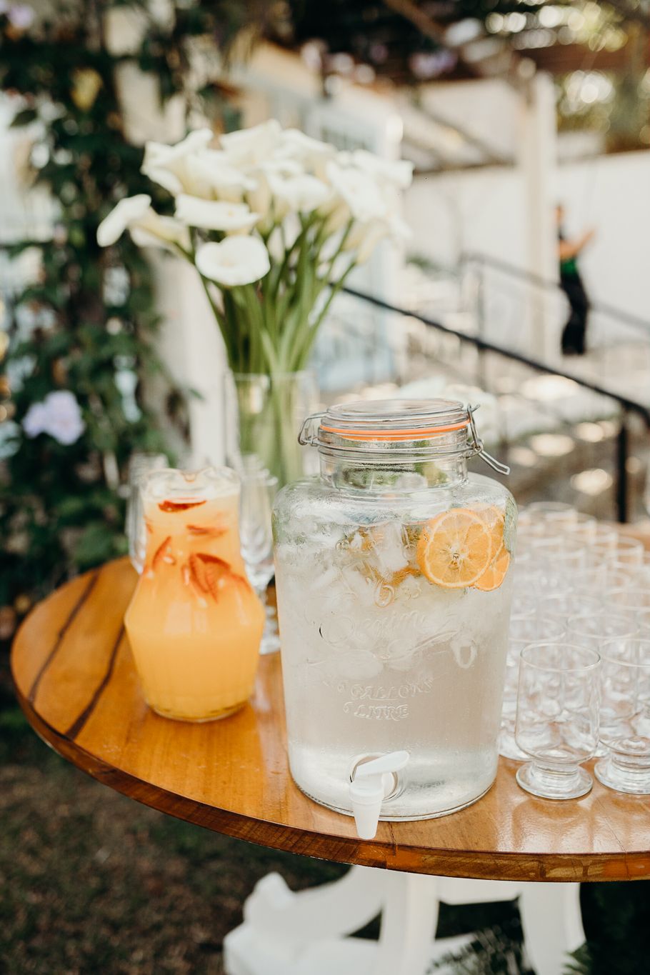 Glass drink dispensers filled with clear and orange beverages on wooden serving tables.