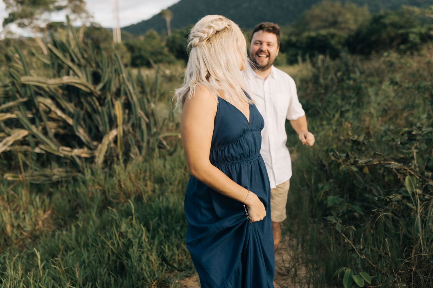 Couple sharing a playful moment on a grassy hillside overlooking the ocean.