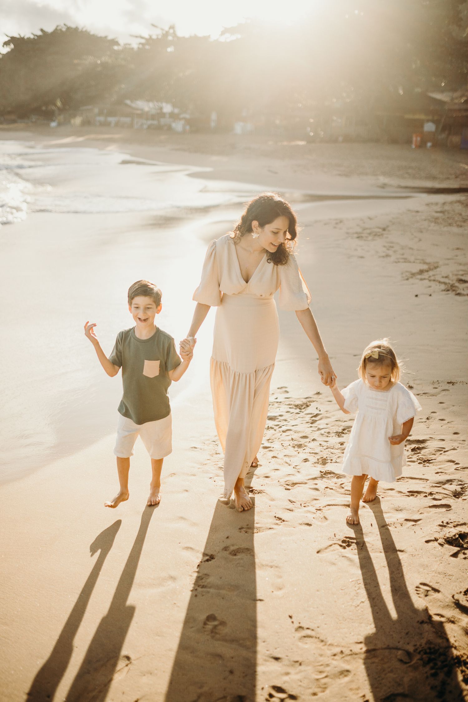 Family walking along beach shoreline casting long shadows at sunset.