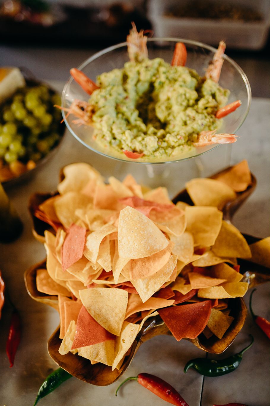 Guacamole garnished with shrimp served alongside colorful tortilla chips and peppers.