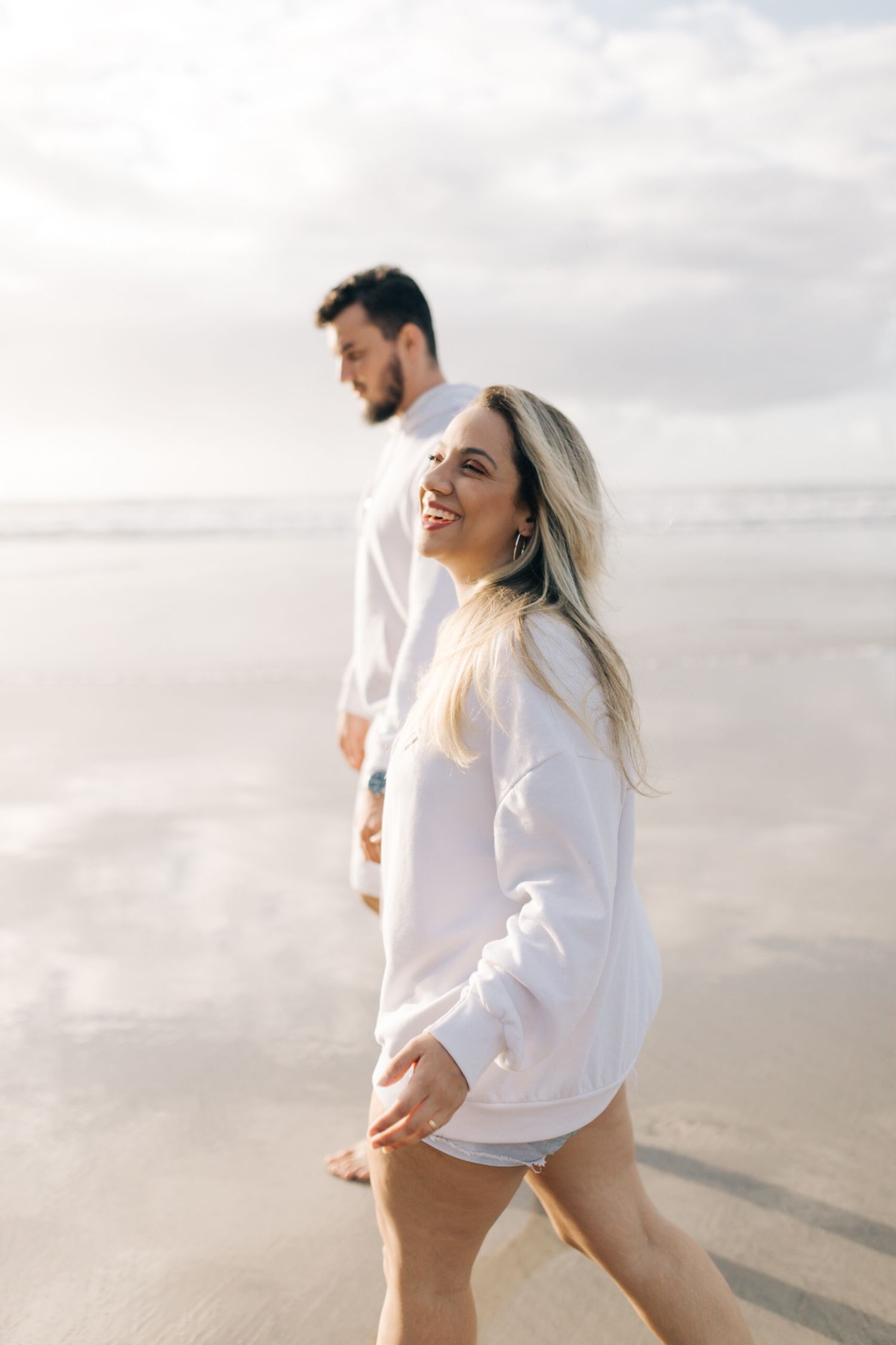 A couple in white sweaters walking together on a misty beach.