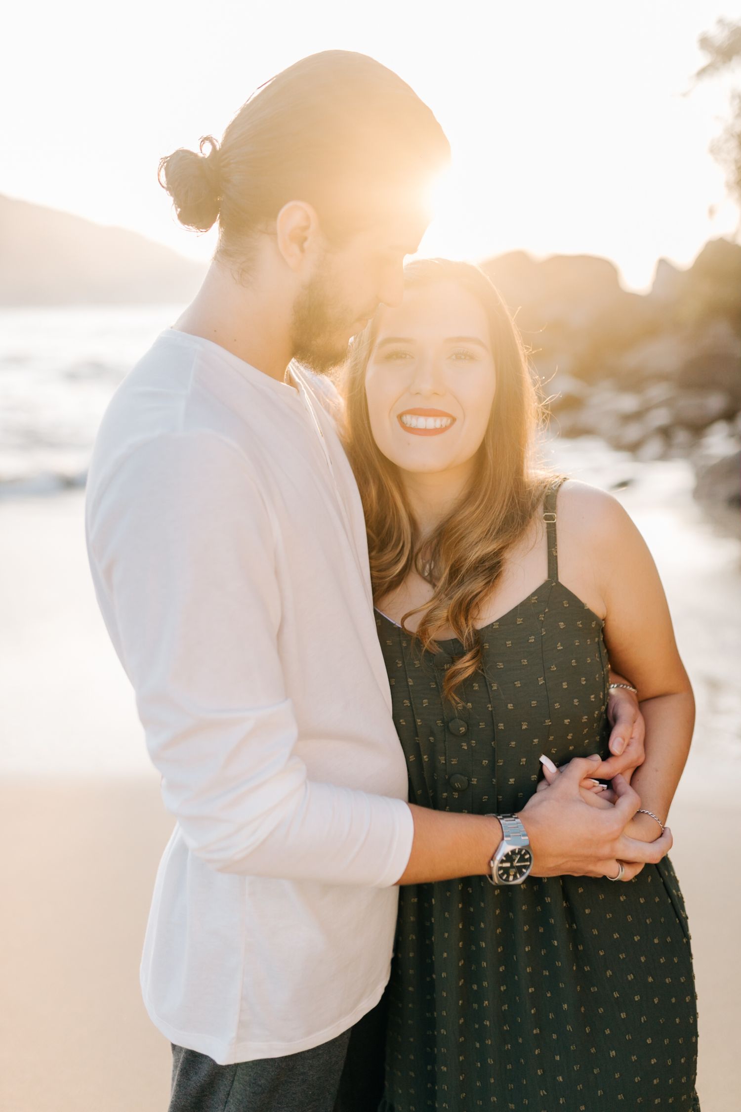 Sunset beach portrait of couple in romantic embrace wearing white shirt and polka dot dress.
