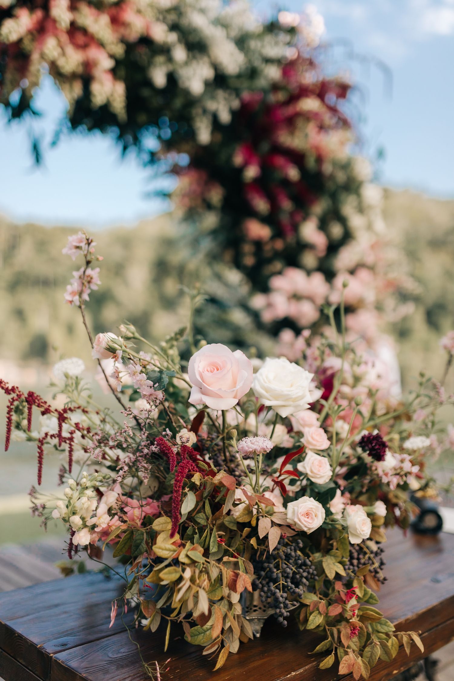 Romantic pink and burgundy floral centerpiece with roses and greenery on wooden table.