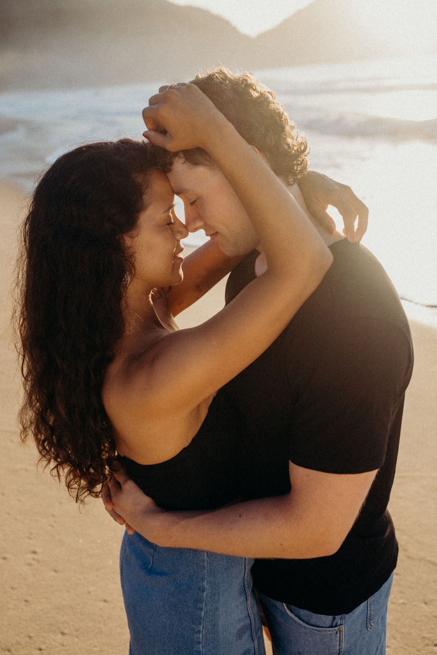 Romantic beach portrait of a couple embracing in warm sunset lighting.