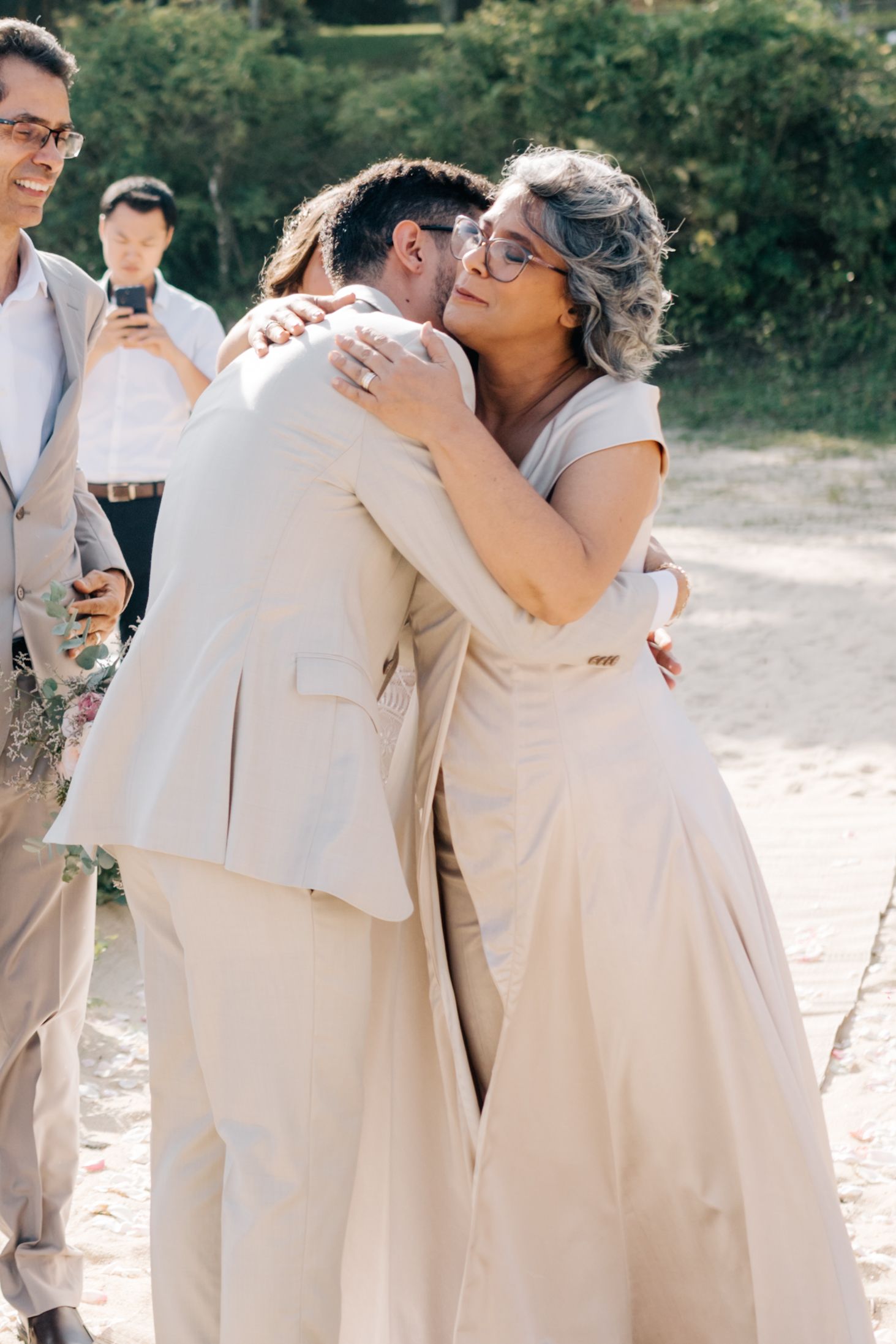 An emotional embrace between wedding attendees wearing light-colored formal attire.