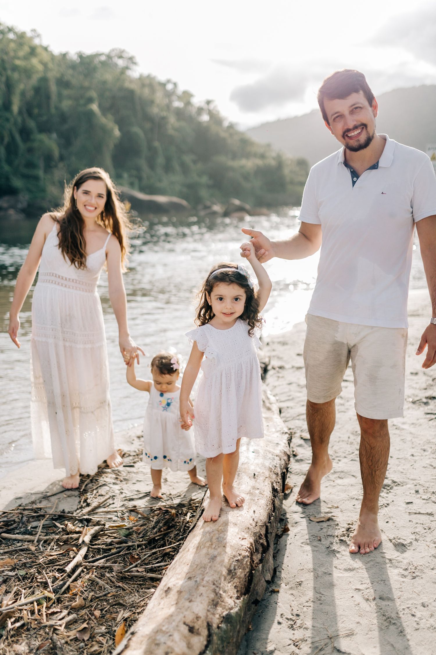 A happy family walks along a beach log during sunset.