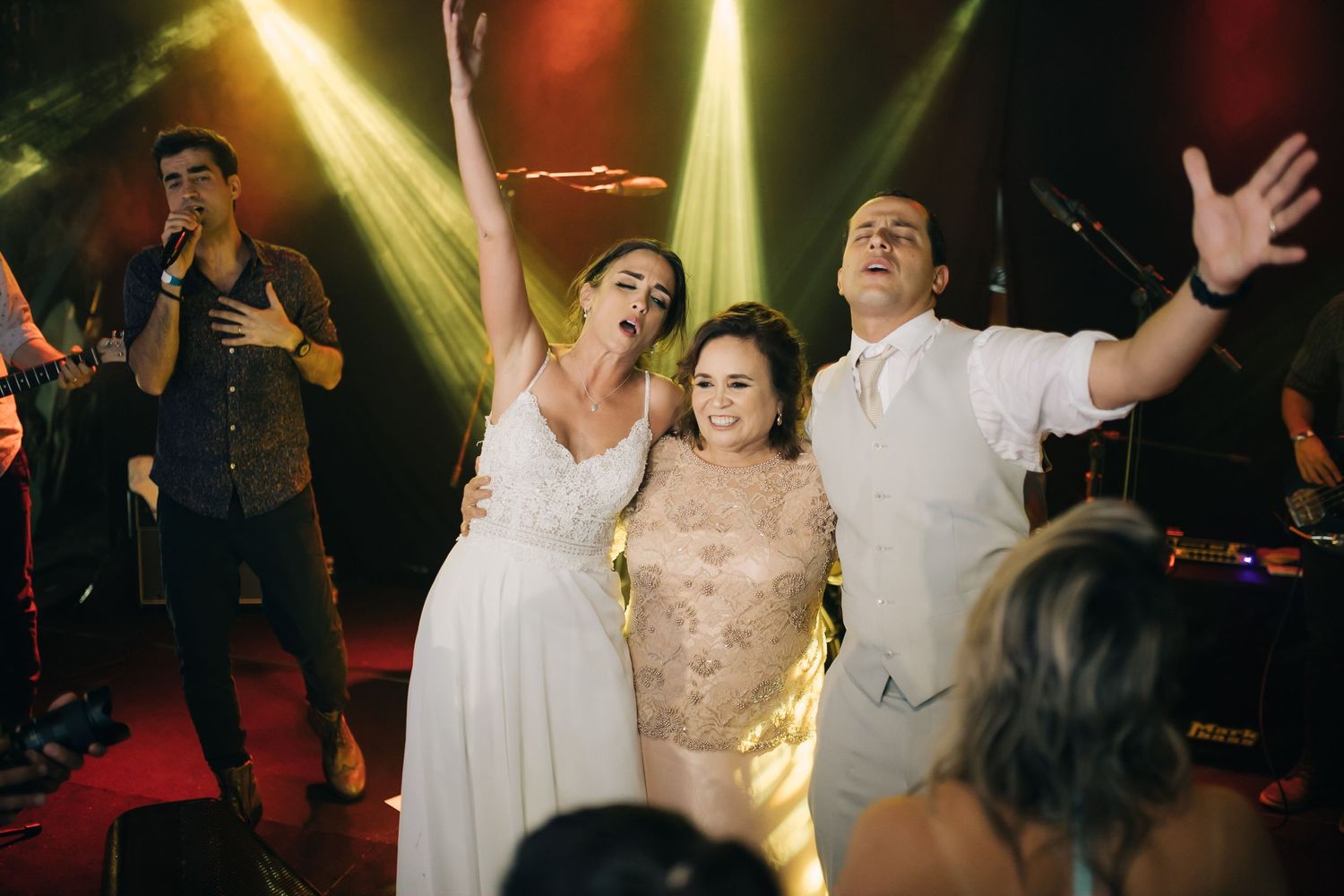 Guests dance enthusiastically together at a wedding reception under colorful spotlights on the dance floor.