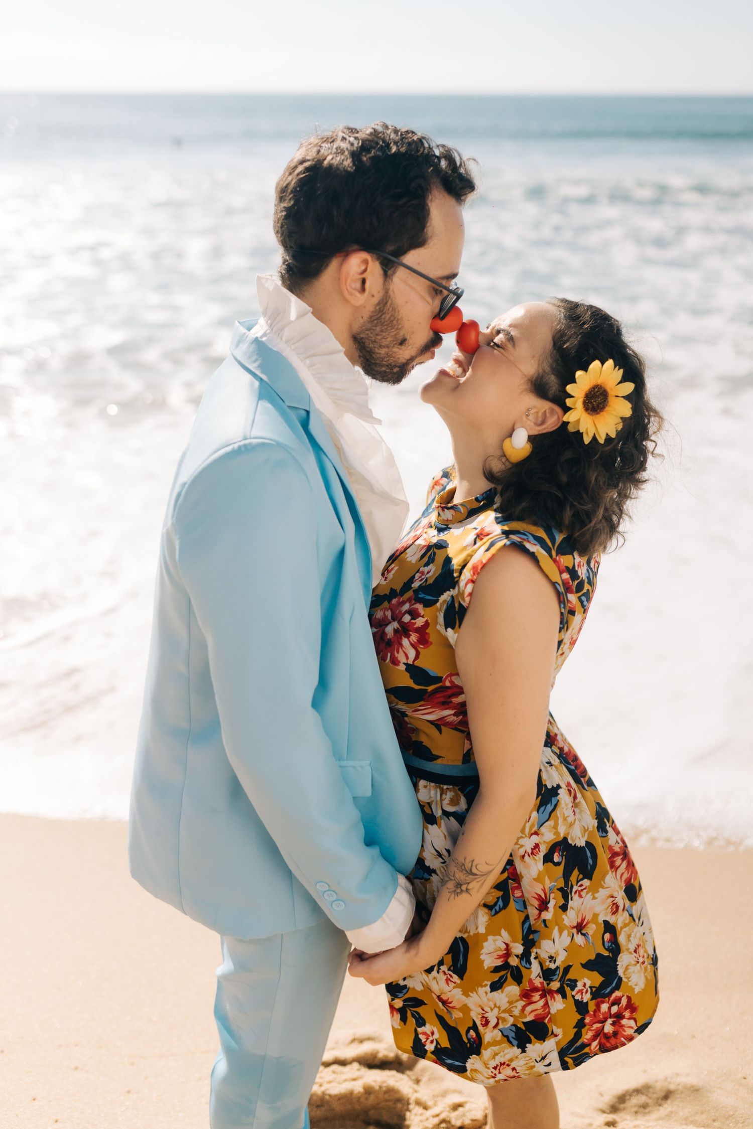 A romantic couple embraces on a sunny beach with waves in the background.