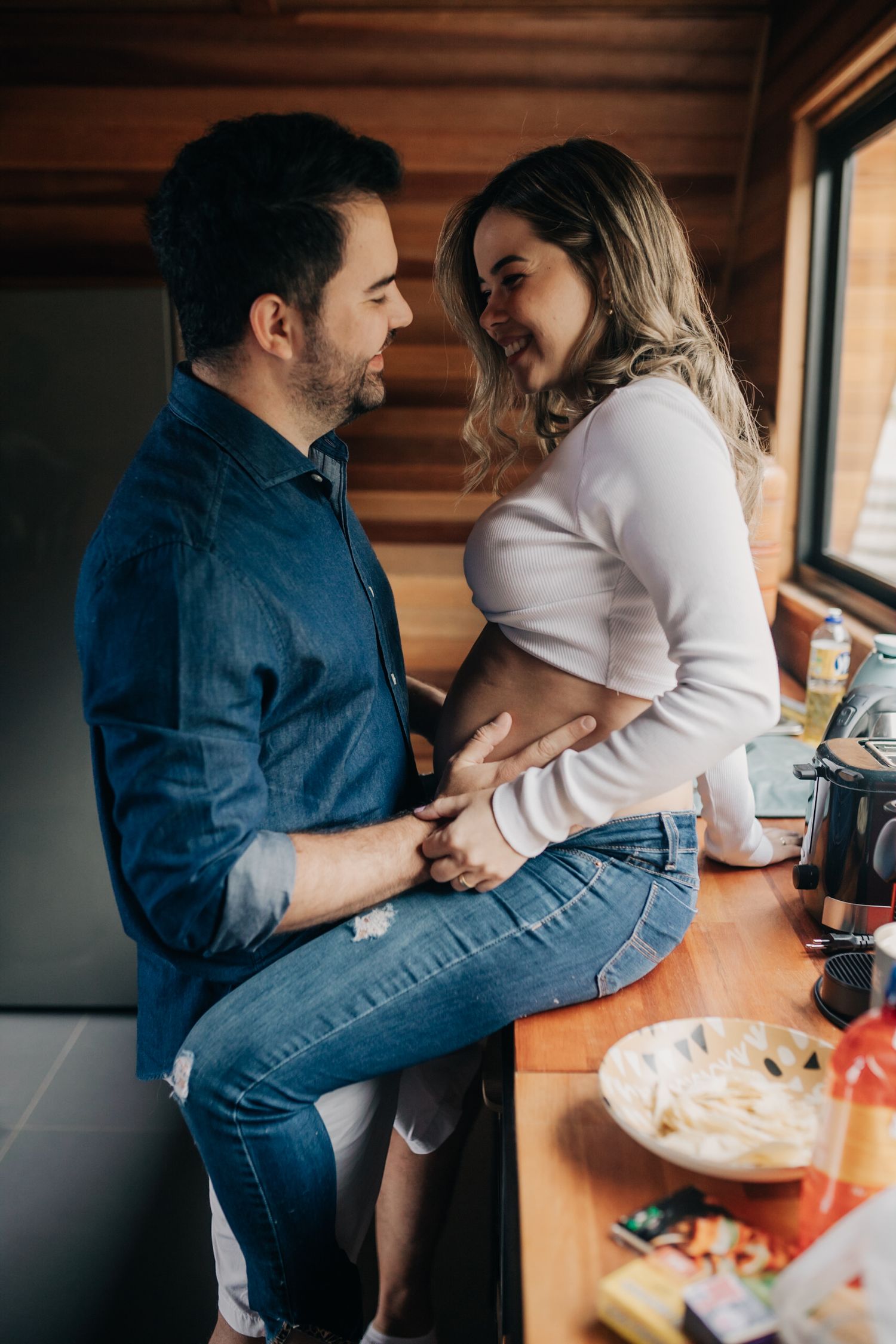 A romantic couple embraces in a cozy cabin kitchen with rustic wooden walls and natural lighting.