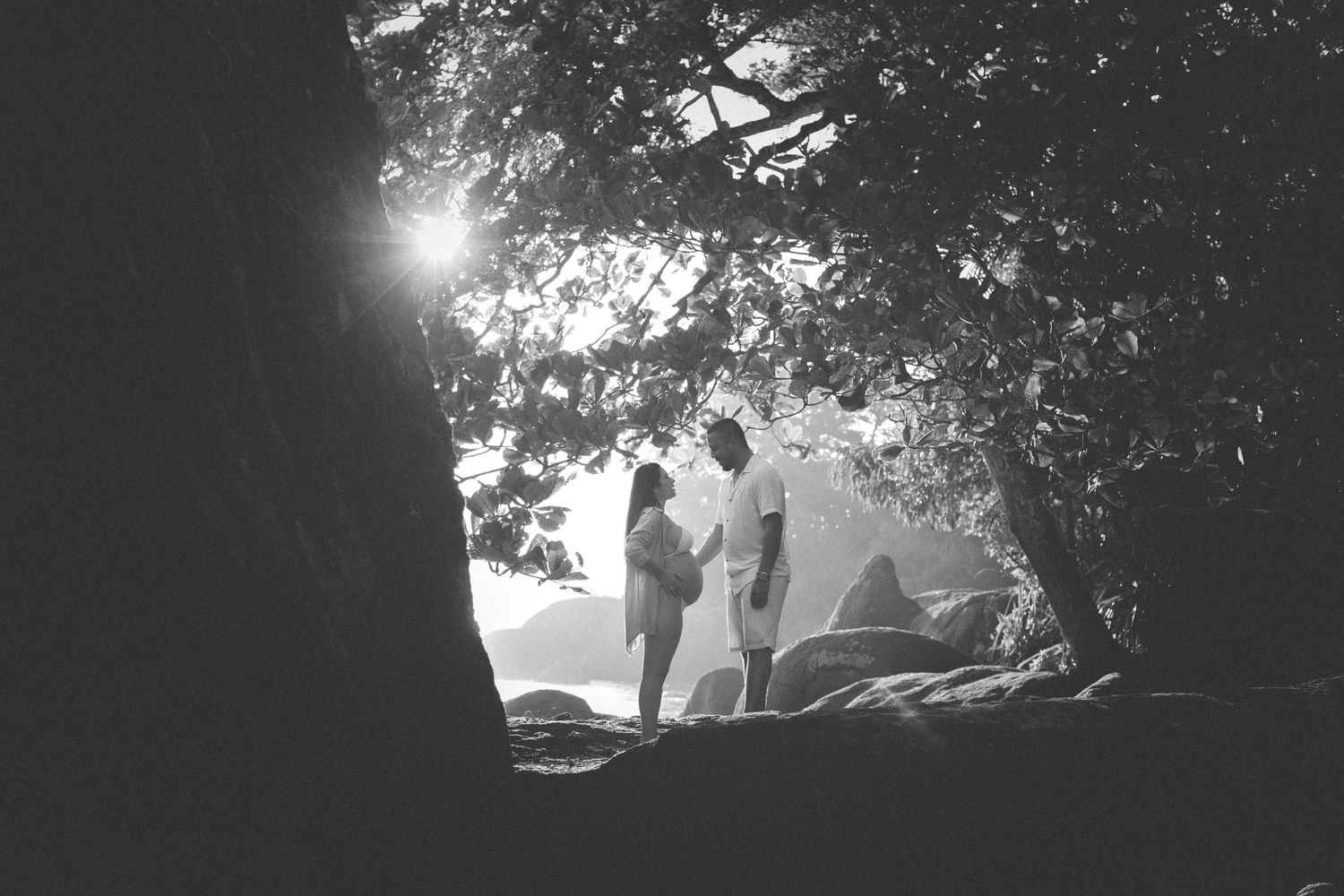 Silhouetted figures stand together against bright sunlight filtering through trees.