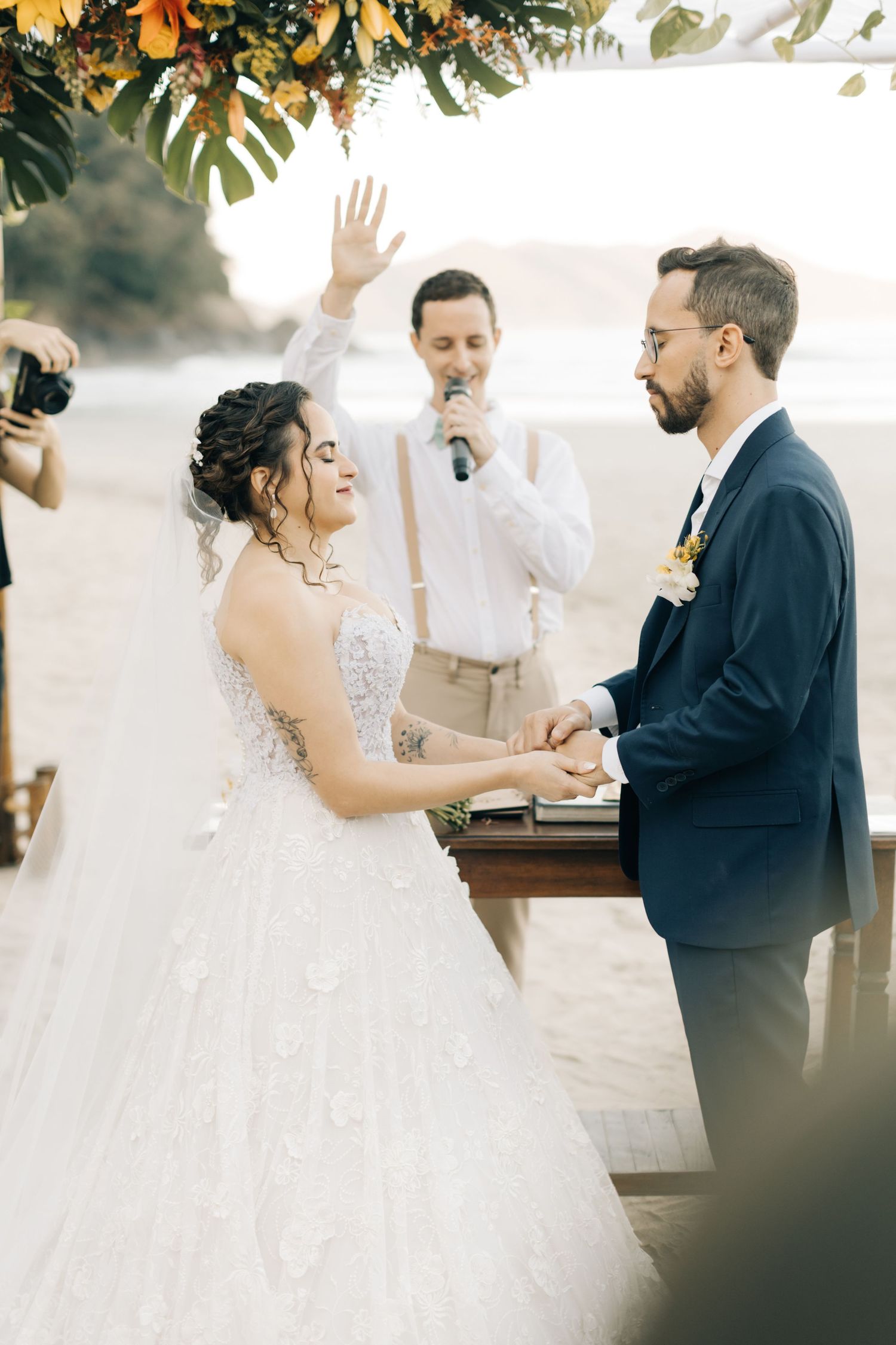 Couple exchanges heartfelt vows under floral arch at beach wedding.