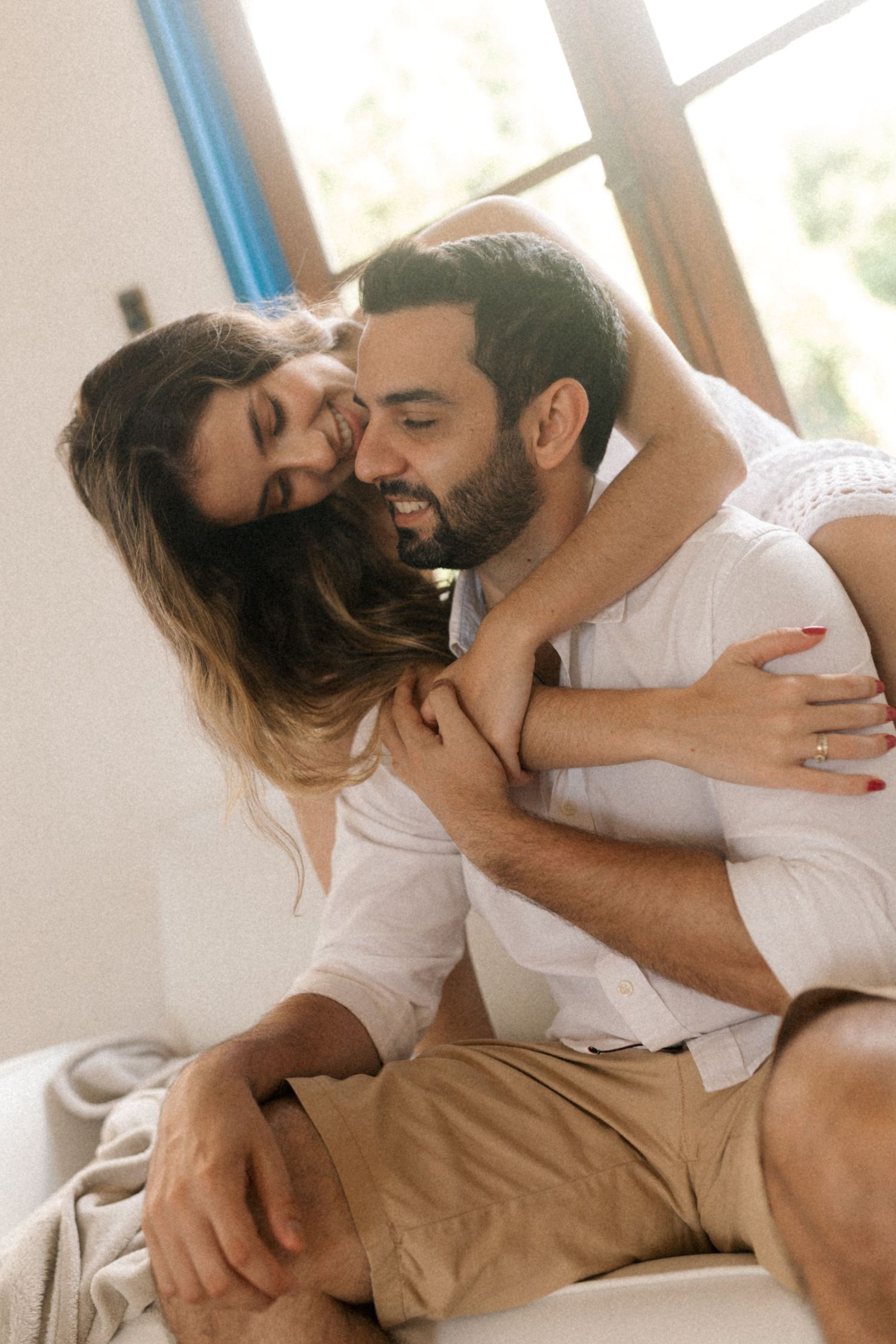 Affectionate couple embracing in a sunlit room with matching white outfits.