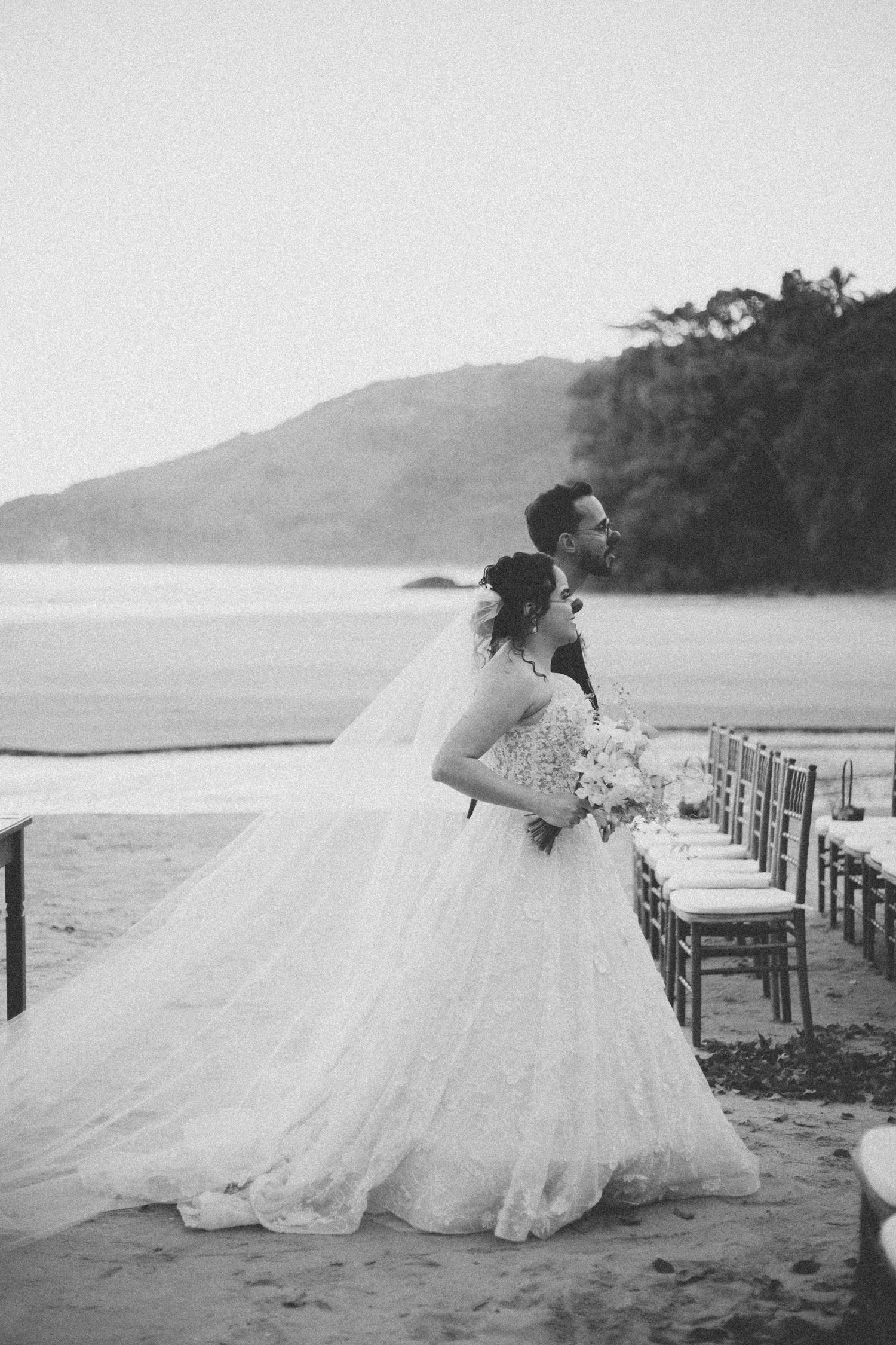 Black and white beach wedding portrait with dramatic mountain backdrop.