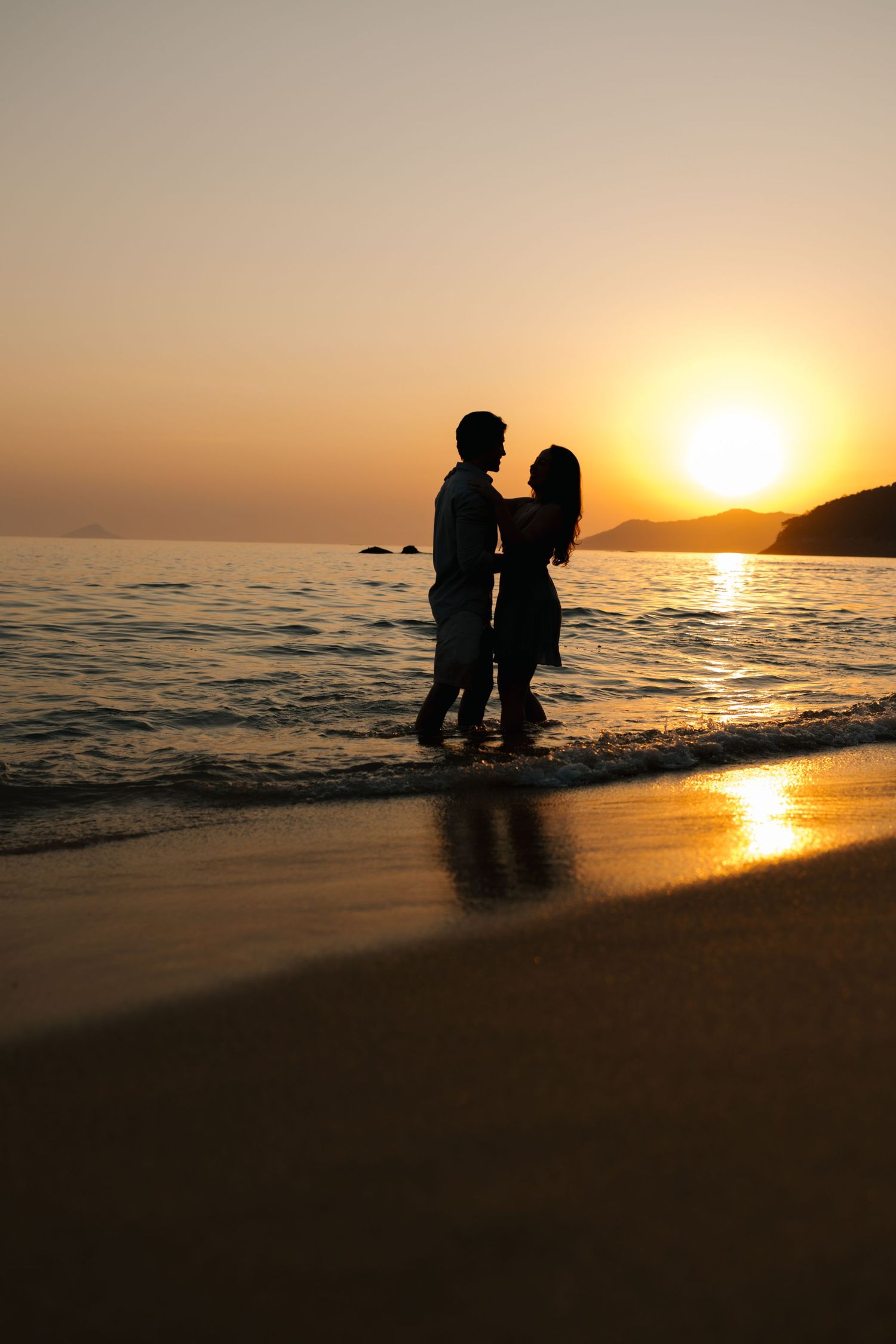 Silhouettes of a couple standing together on beach during golden sunset.