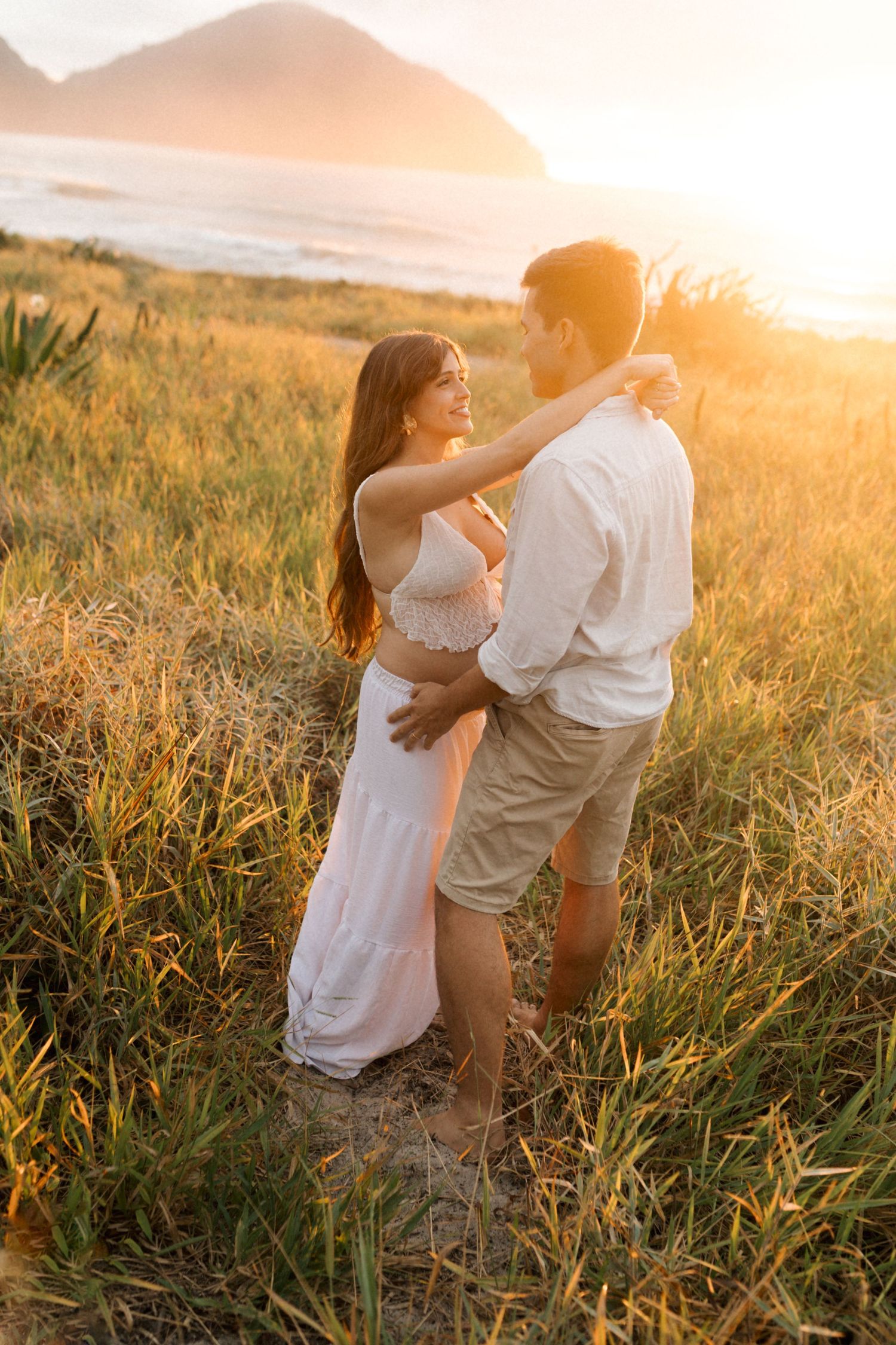 Romantic couple dancing and embracing in a golden field at sunset with flowing white dress and gentle movement.