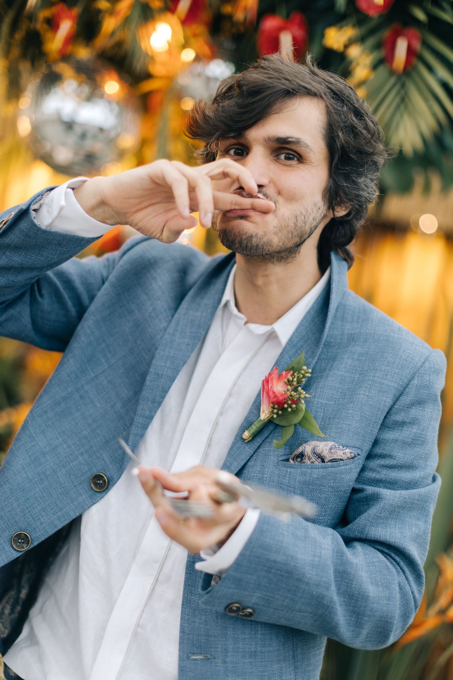 Guest in blue suit enjoying dessert at wedding reception with tropical decorations.