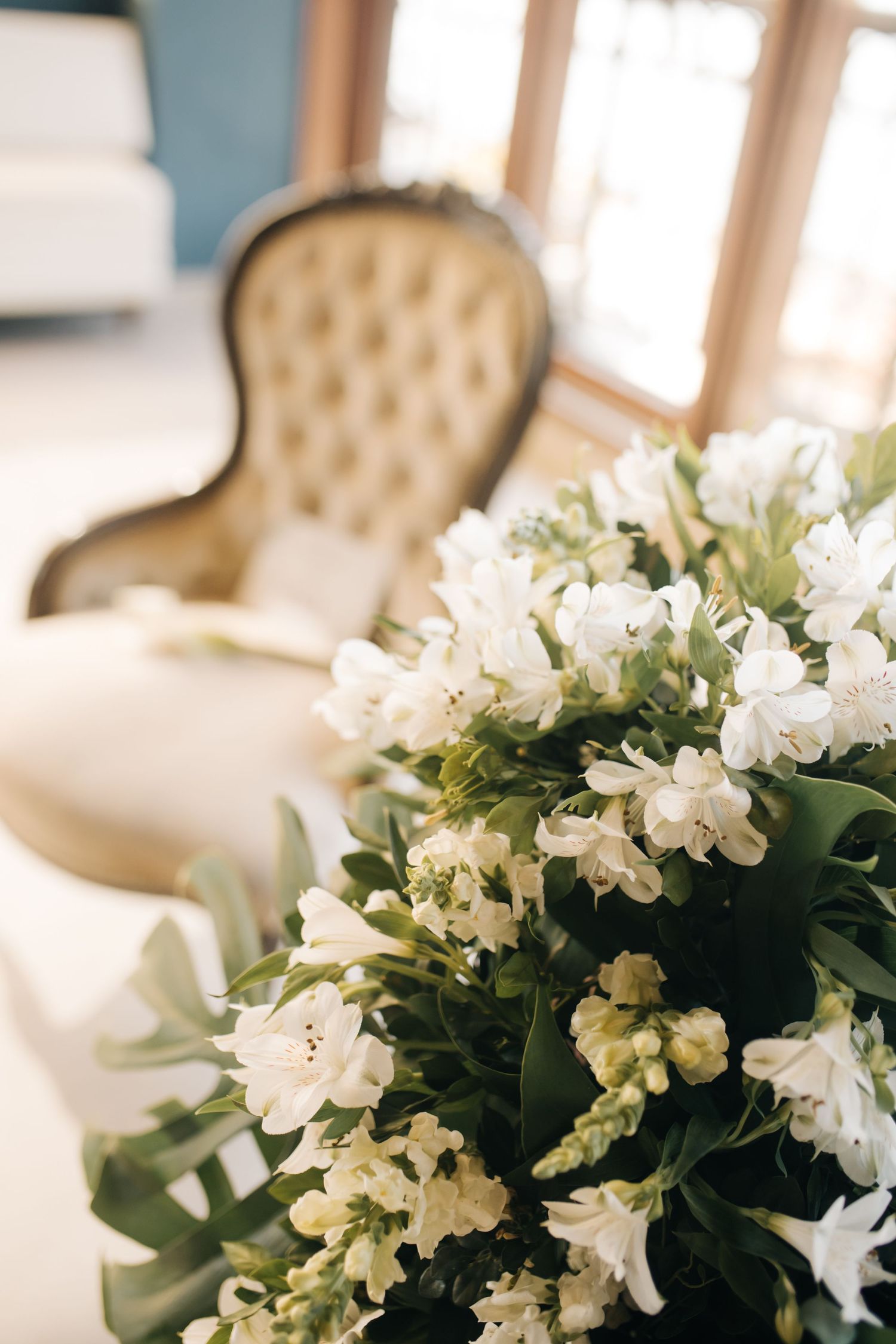 Close-up of white floral arrangement with vintage tufted chair in background.