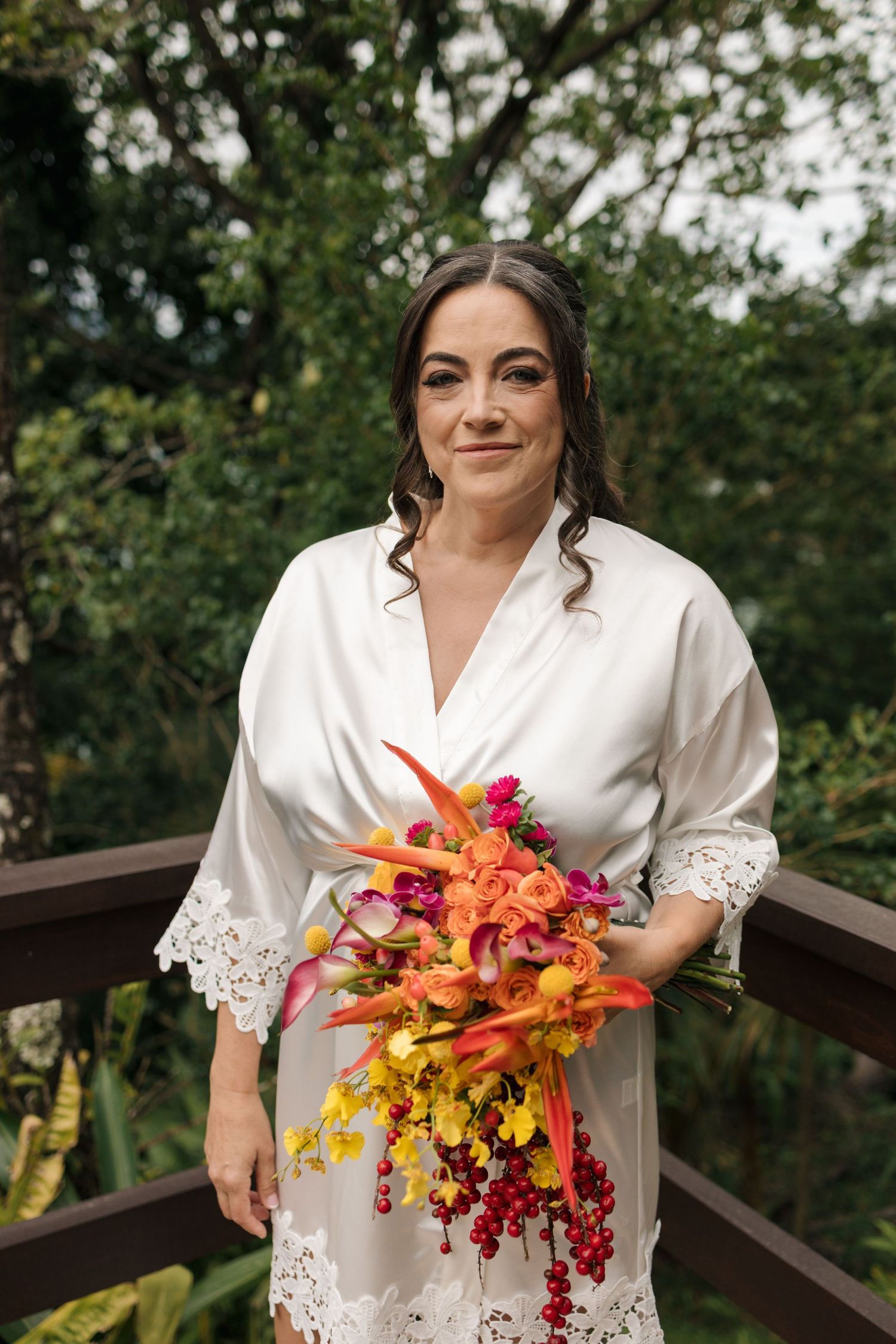 Someone wearing a white lace-trimmed robe holds a vibrant autumn-colored bouquet outdoors.