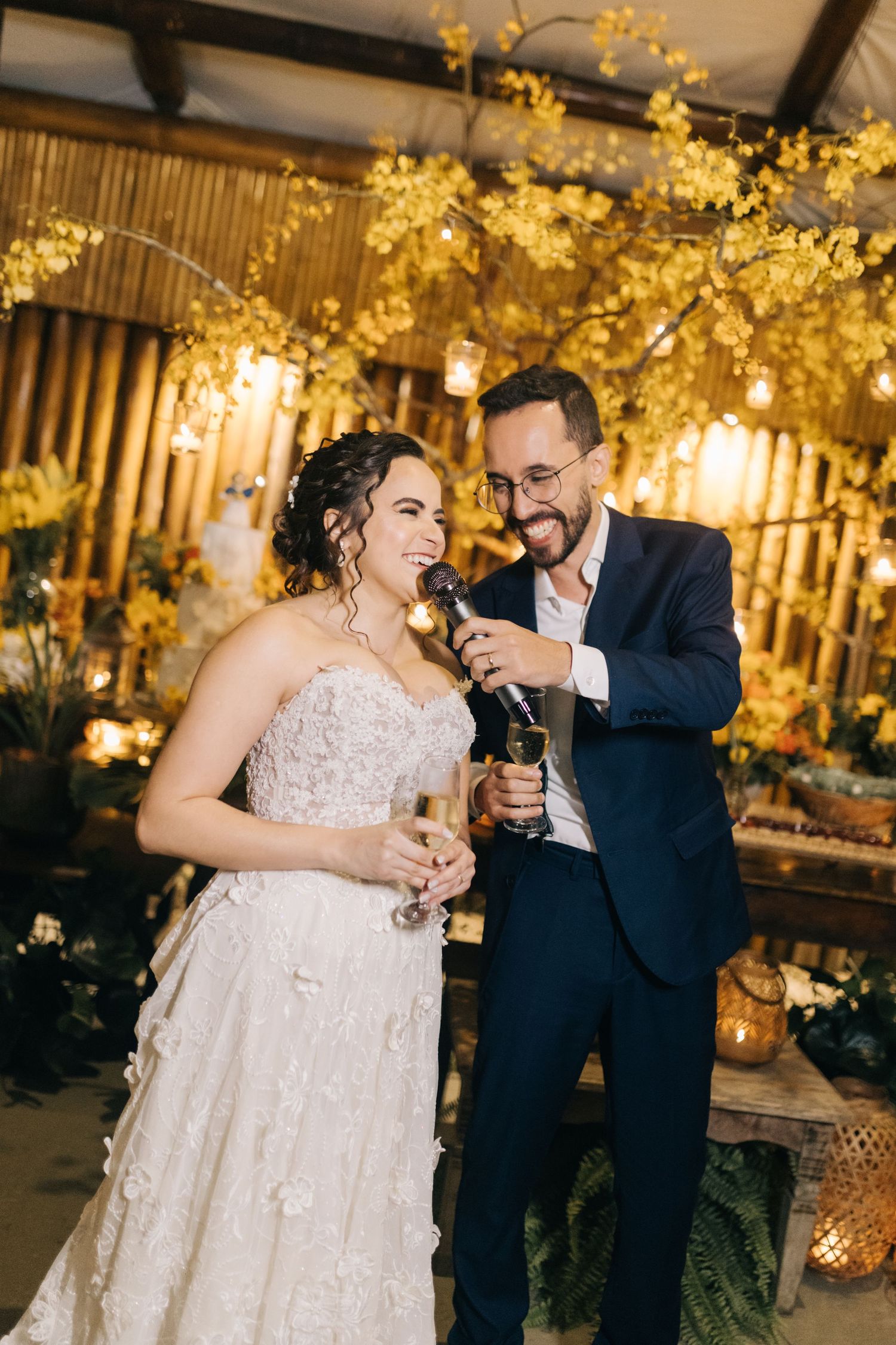 Newlyweds share a joyful moment under warm golden lighting and floral decorations.