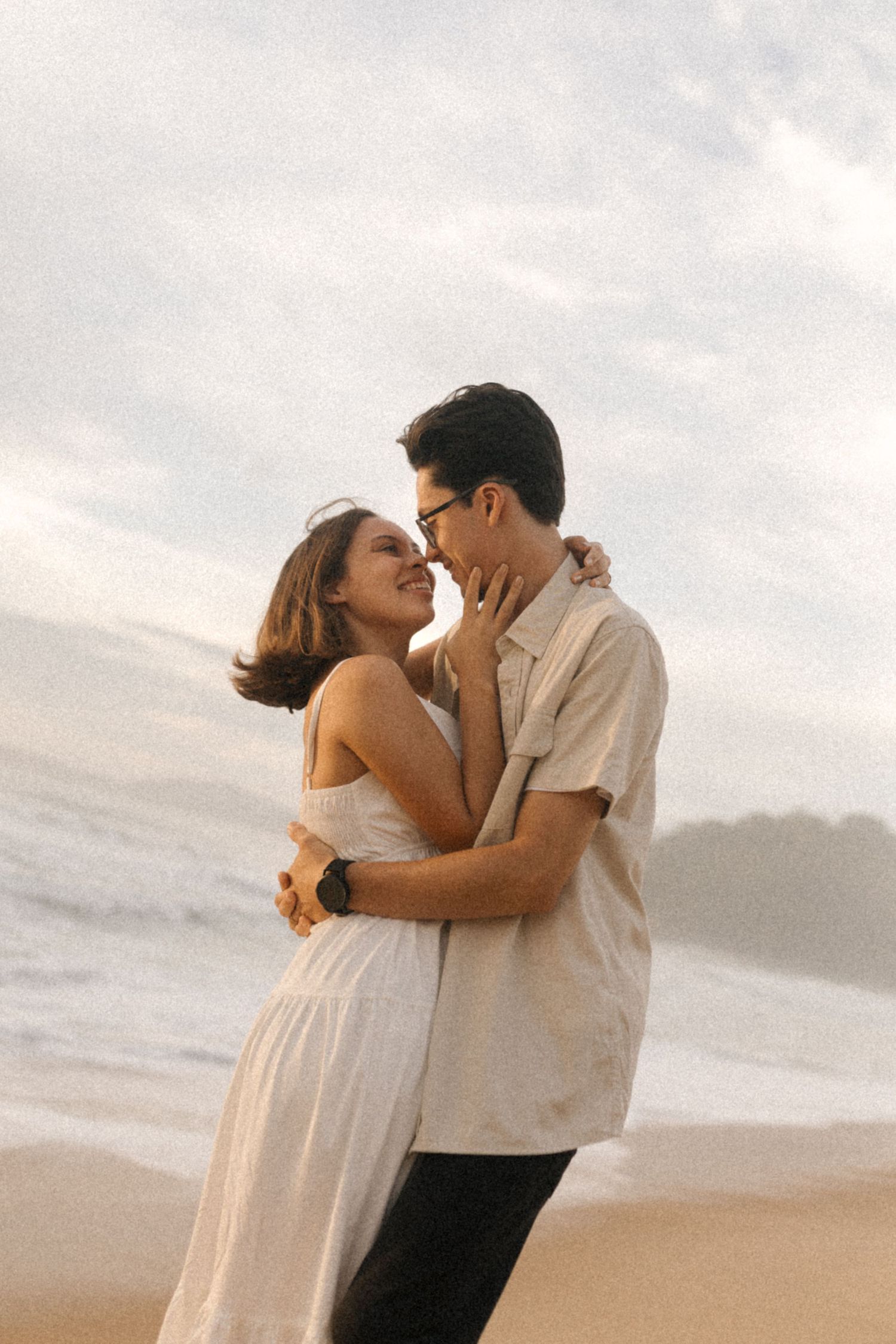 A romantic couple embraces and shares a tender kiss on a serene beach at sunset.