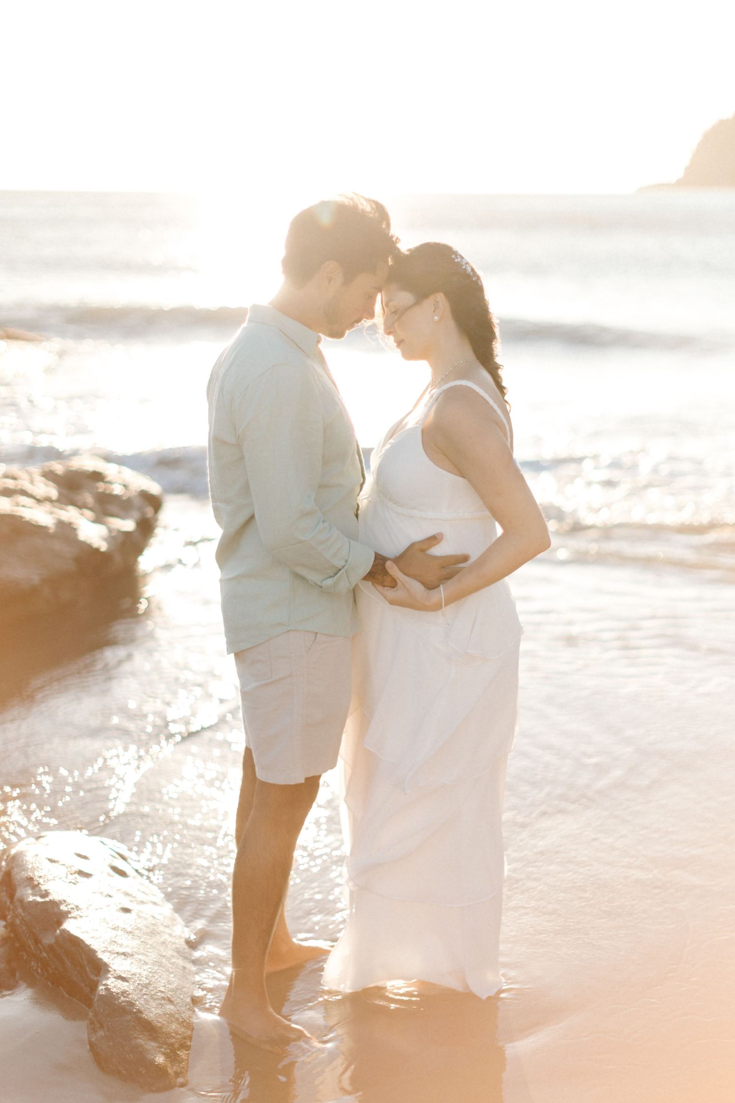 Couple sharing a tender moment on the beach at sunset with waves rolling in.